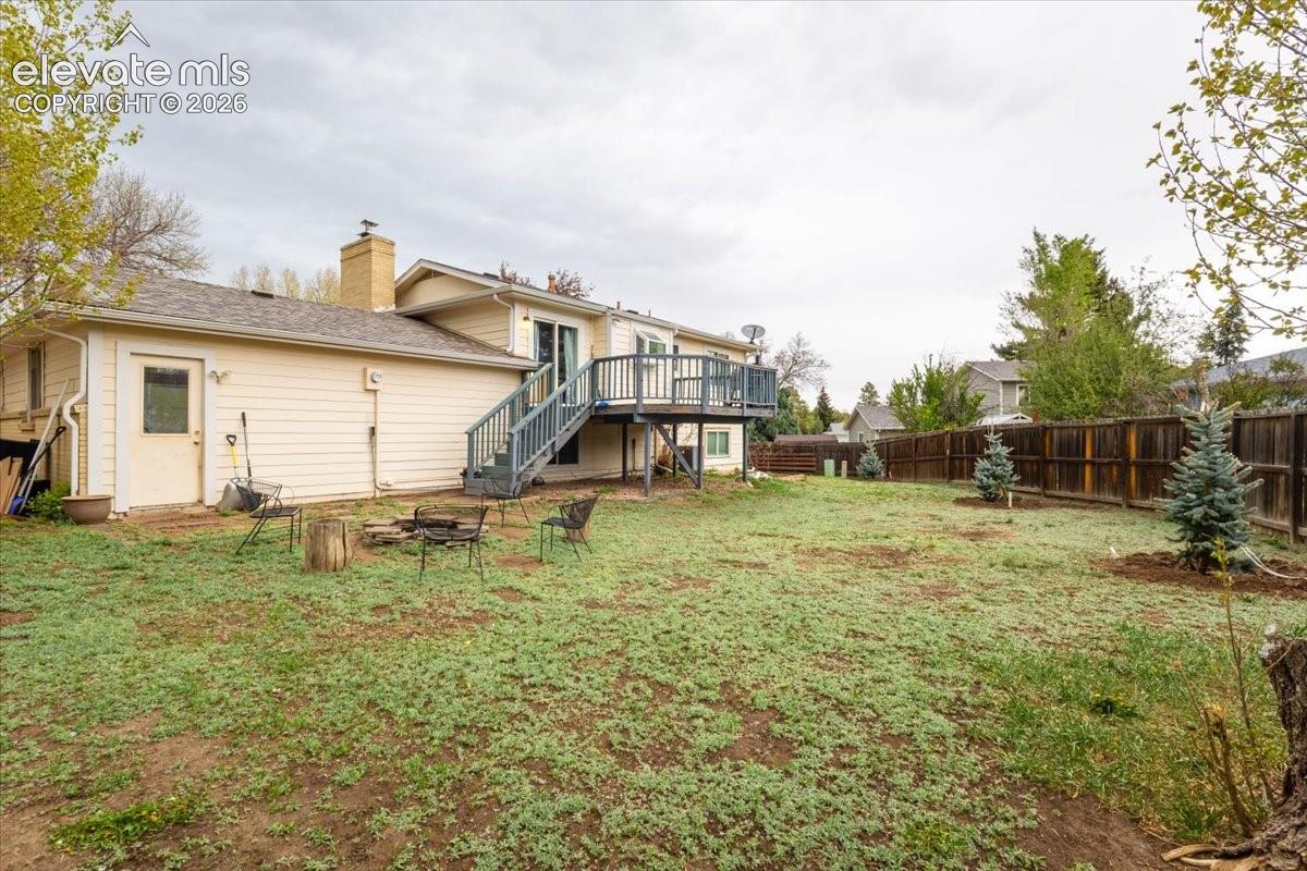 Spacious backyard featuring a multi-level deck with stairs, a privacy fence, and multiple young evergreen trees