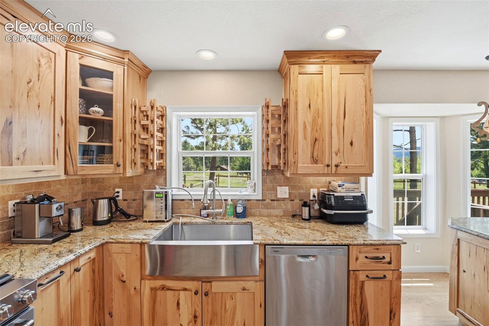 Kitchen featuring natural wood cabinetry, granite countertops, a stainless steel farmhouse sink, and a tiled backsplash