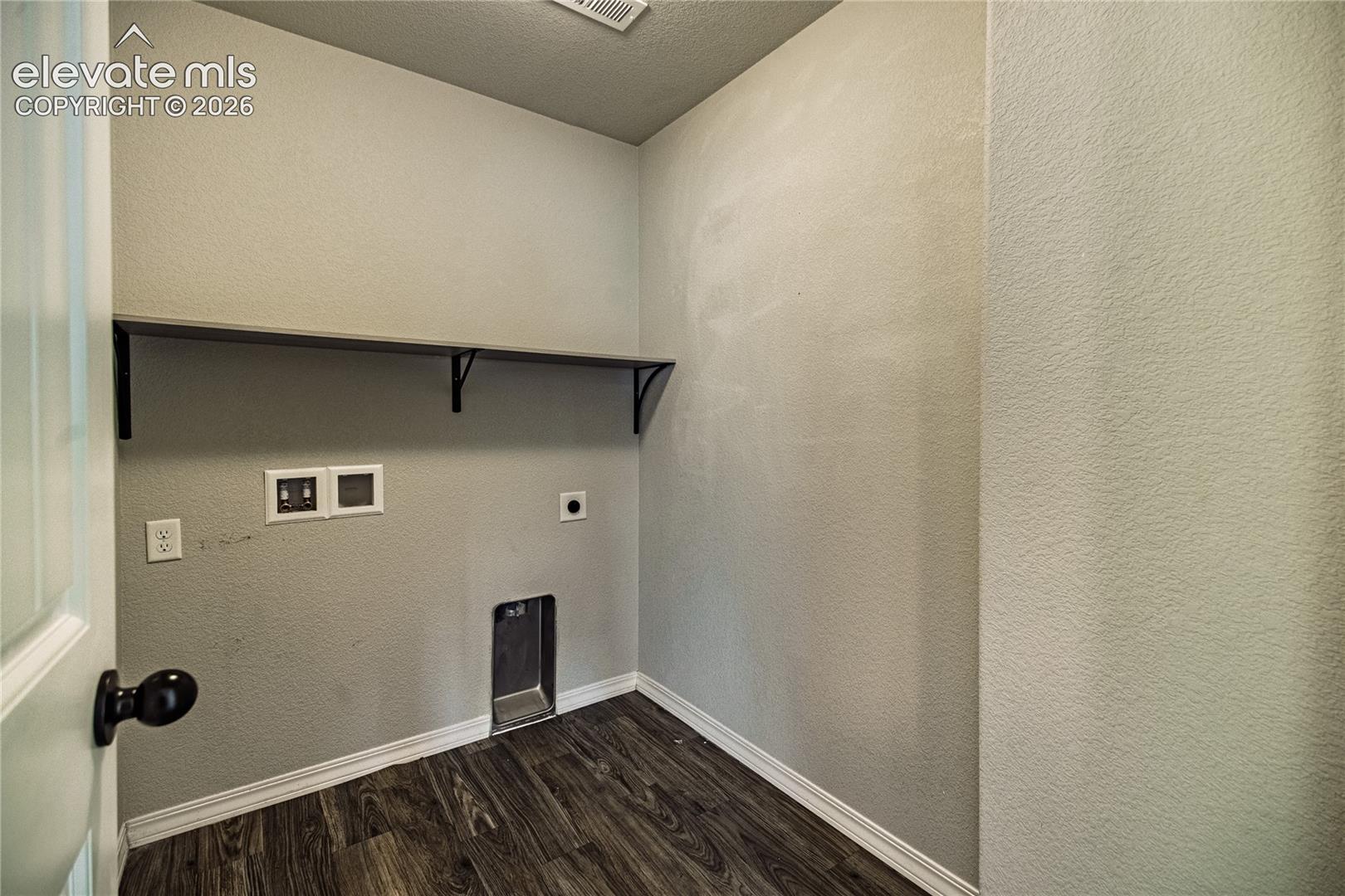 Dedicated utility space featuring a built-in shelf with supports and dark wood-finish flooring