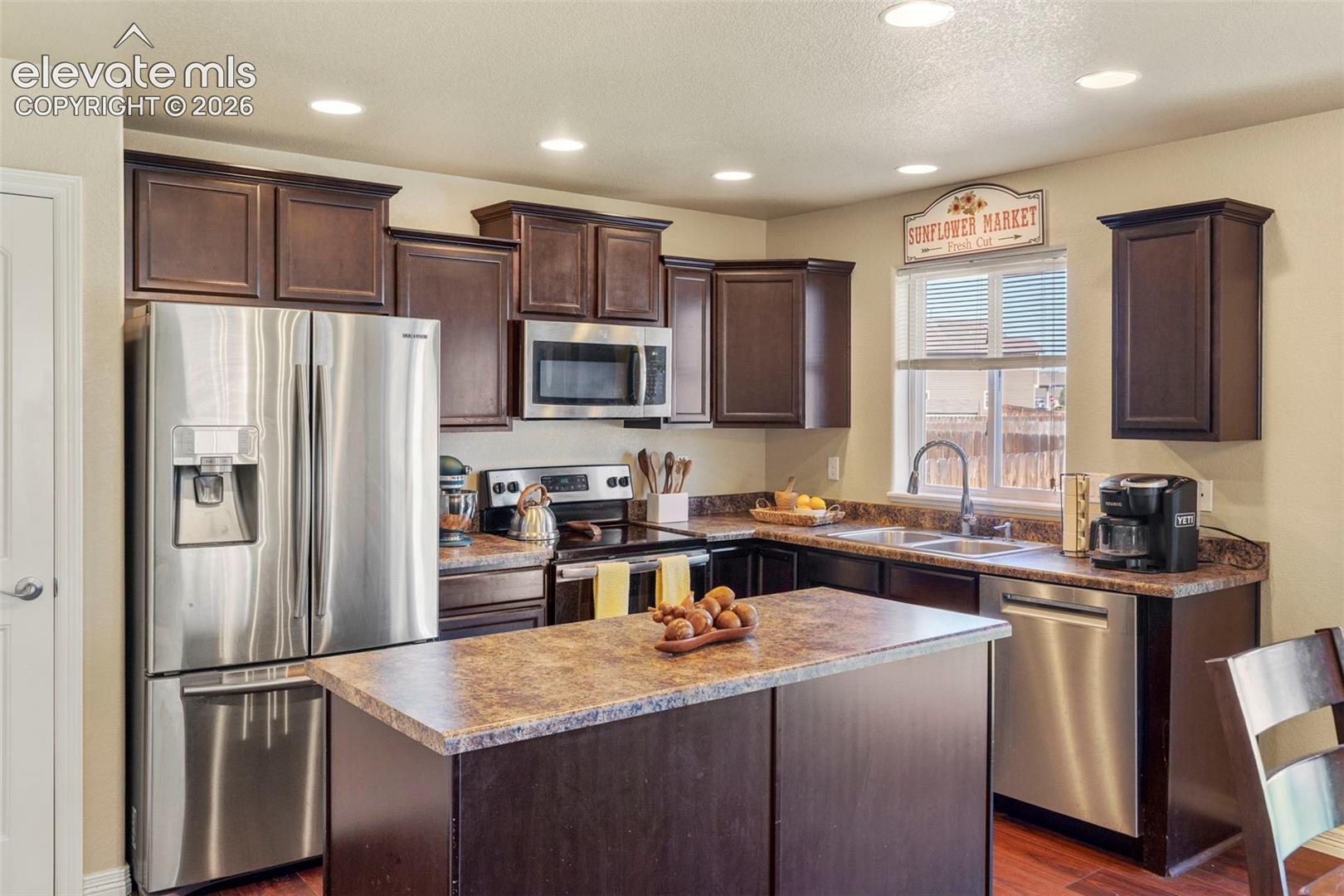 Kitchen featuring dark wood cabinetry, stainless steel appliances, a center island with a stone-finish countertop, and recessed lighting