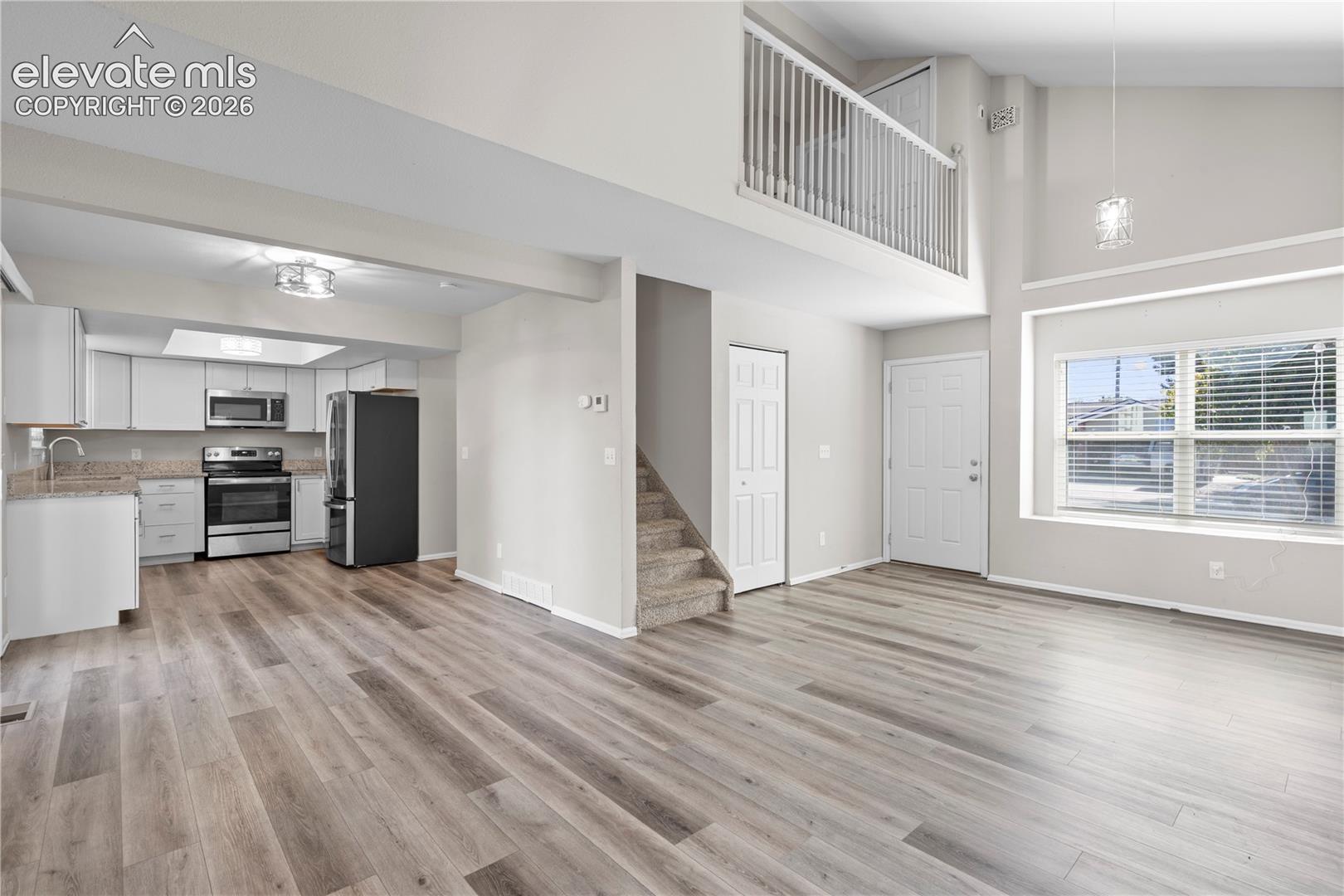 Vaulted ceilings, wood-finish flooring, white cabinetry, stone-finish countertops, and an elevated interior balcony railing