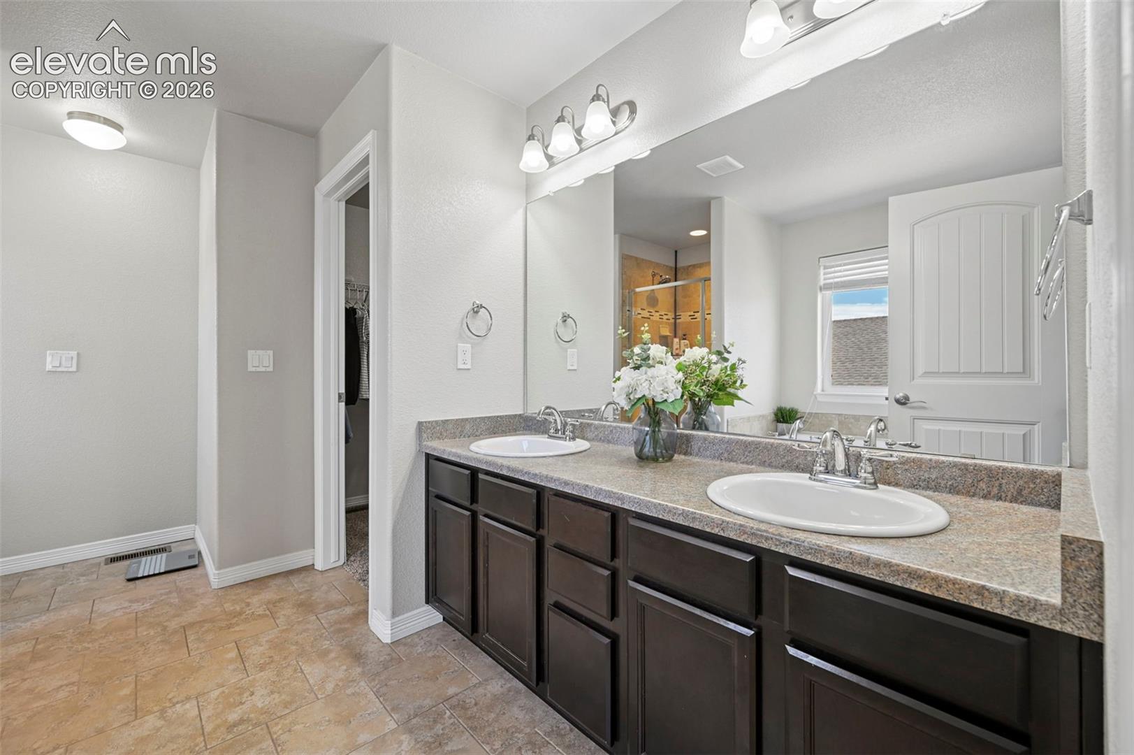 Dual sink vanity with dark wood-finish cabinetry, light-toned countertop, and large wall-mounted mirror