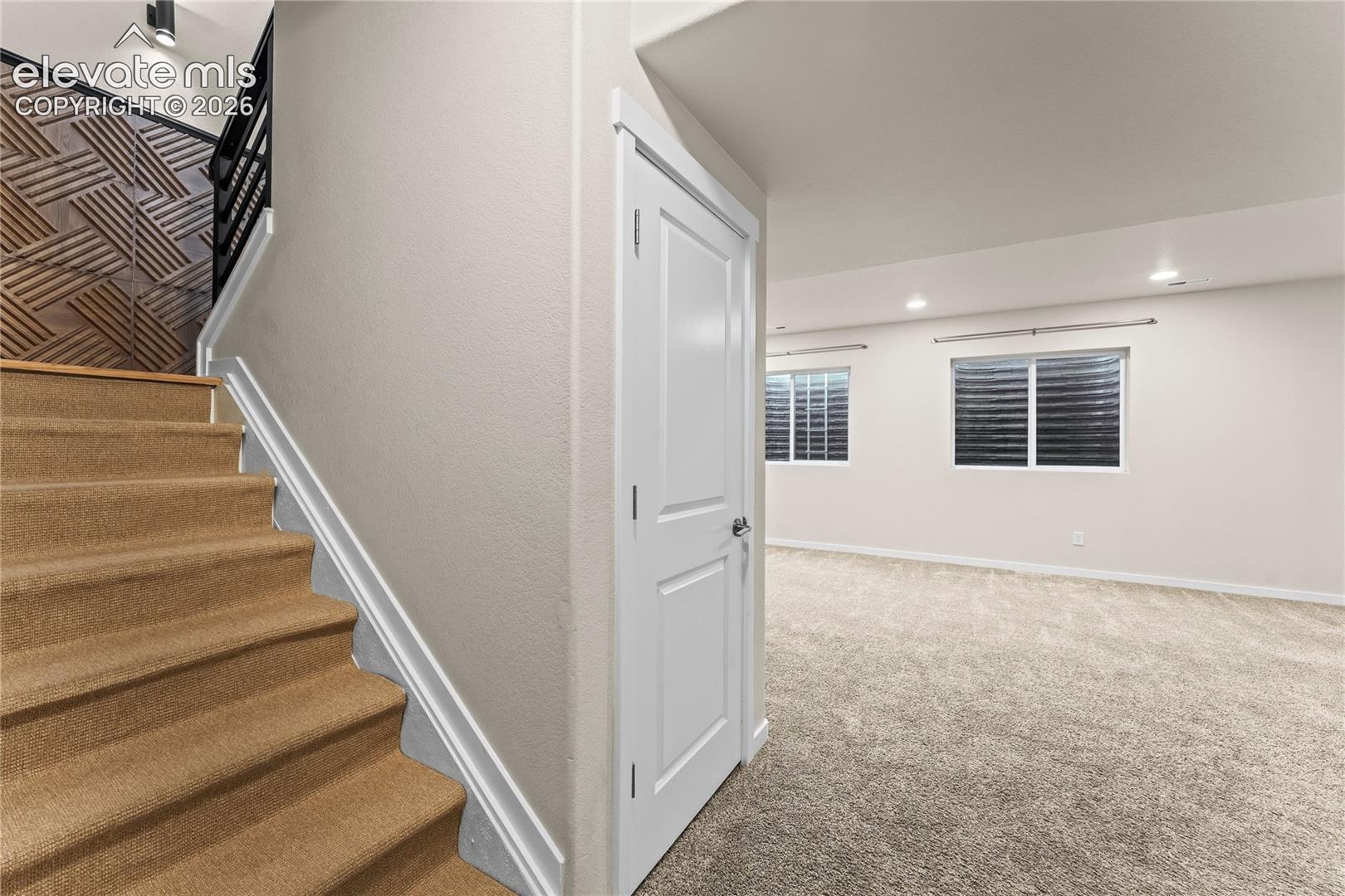 Staircase with carpeted steps and decorative geometric wood wall paneling, featuring a black metal railing and neutral carpeting