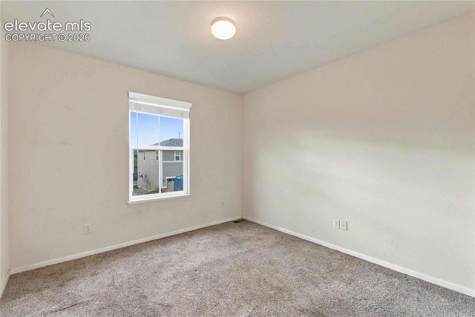 Neutral-toned walls, wall-to-wall carpeting, and a single-hung window with fitted blinds and a flush-mount overhead light fixture