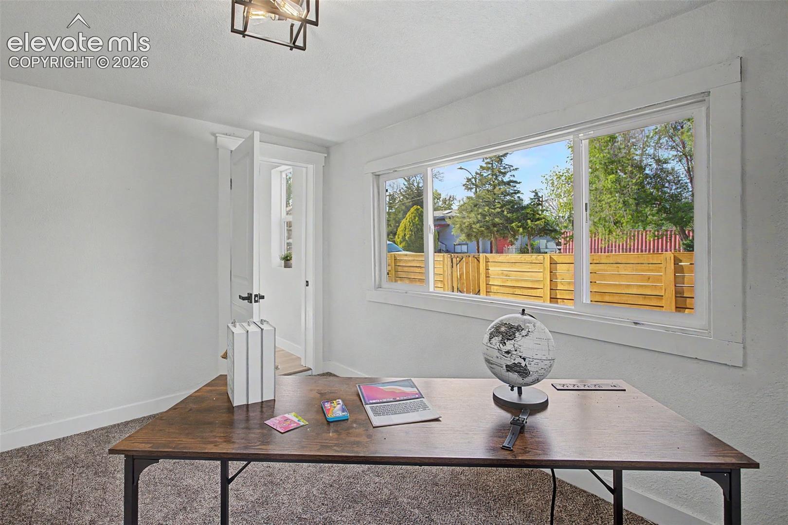 Bright room featuring a large horizontal window, white trim, light-toned walls, and dark textured carpeting