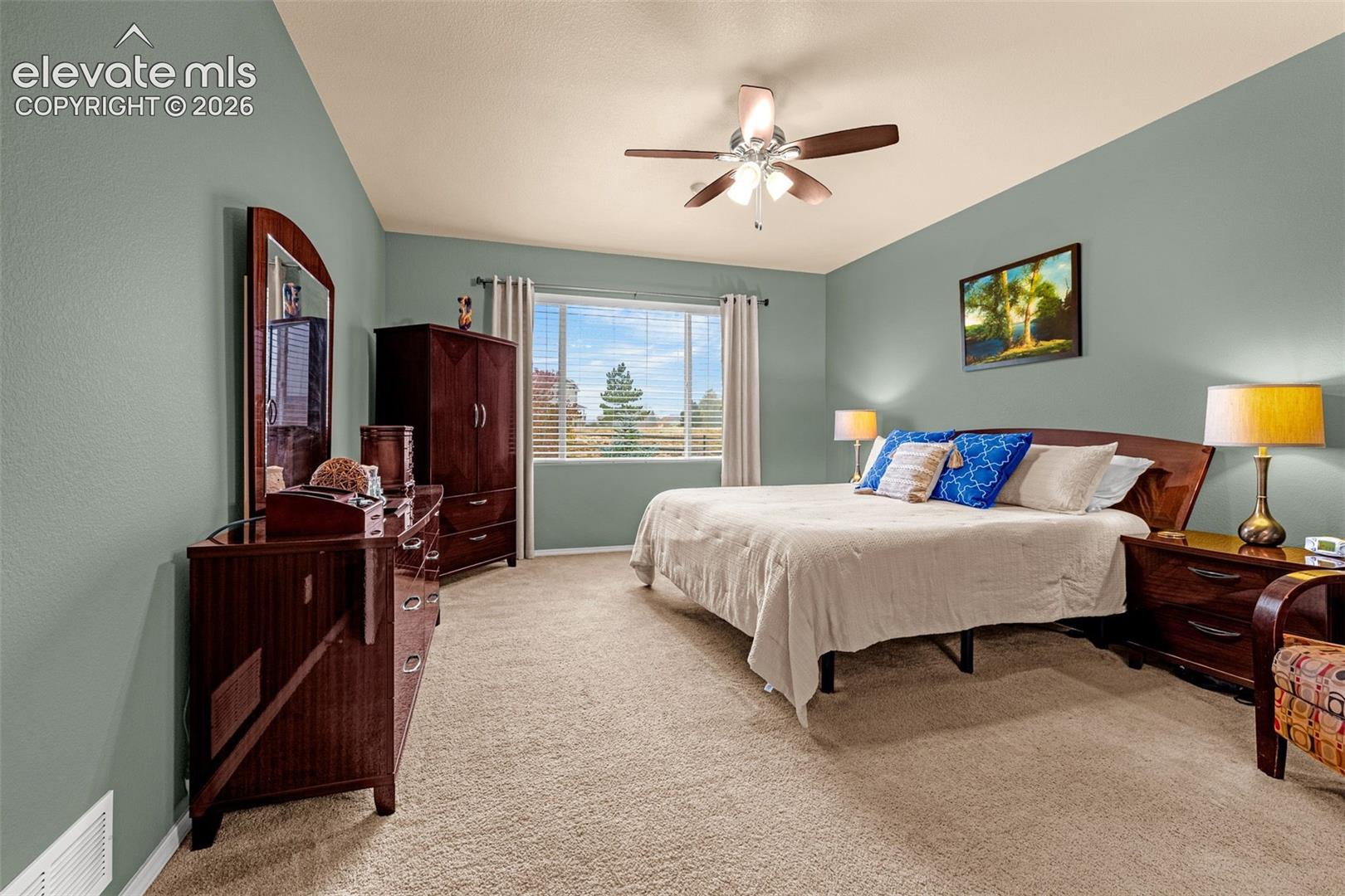 Spacious room featuring neutral carpeting, a dual-tone ceiling fan with integrated lighting, and large windows
