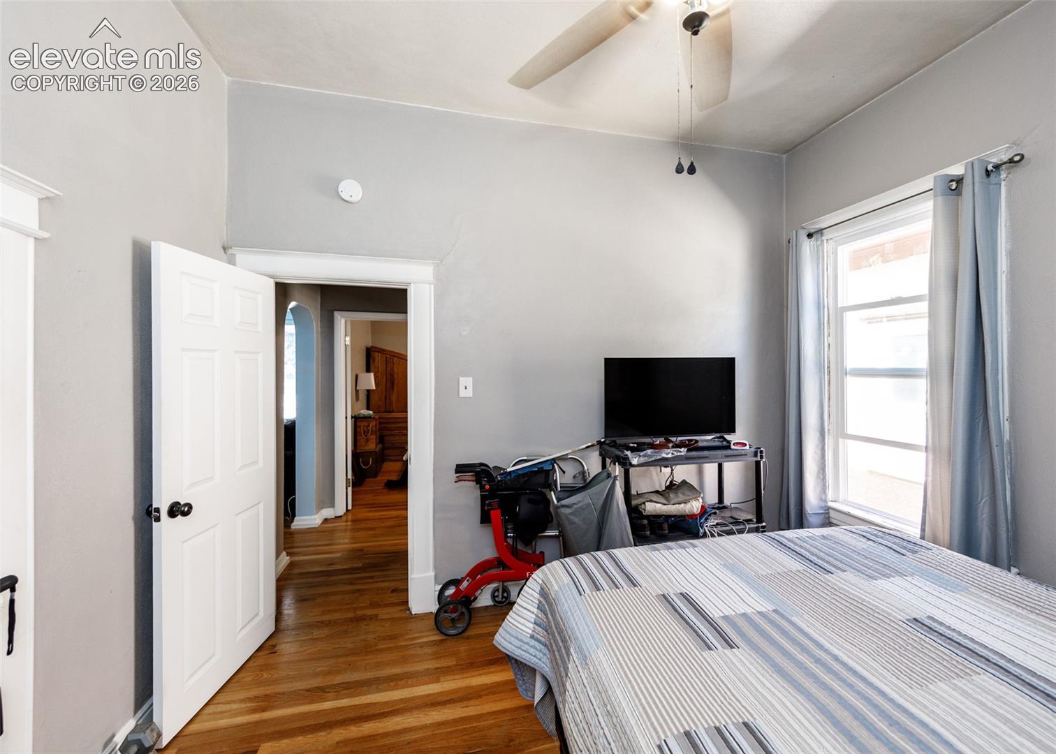 Hardwood flooring, multi-pane window, white trim, ceiling fan, and paneled interior door