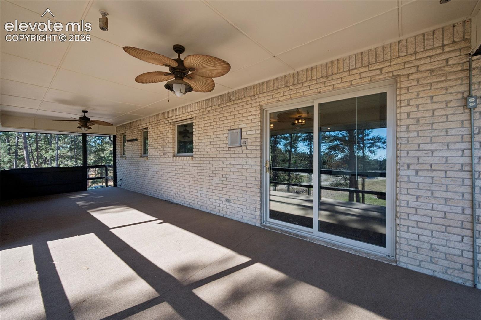 Covered patio featuring a light-colored brick exterior wall, dual ceiling fans, sliding glass doors, and a screen enclosure