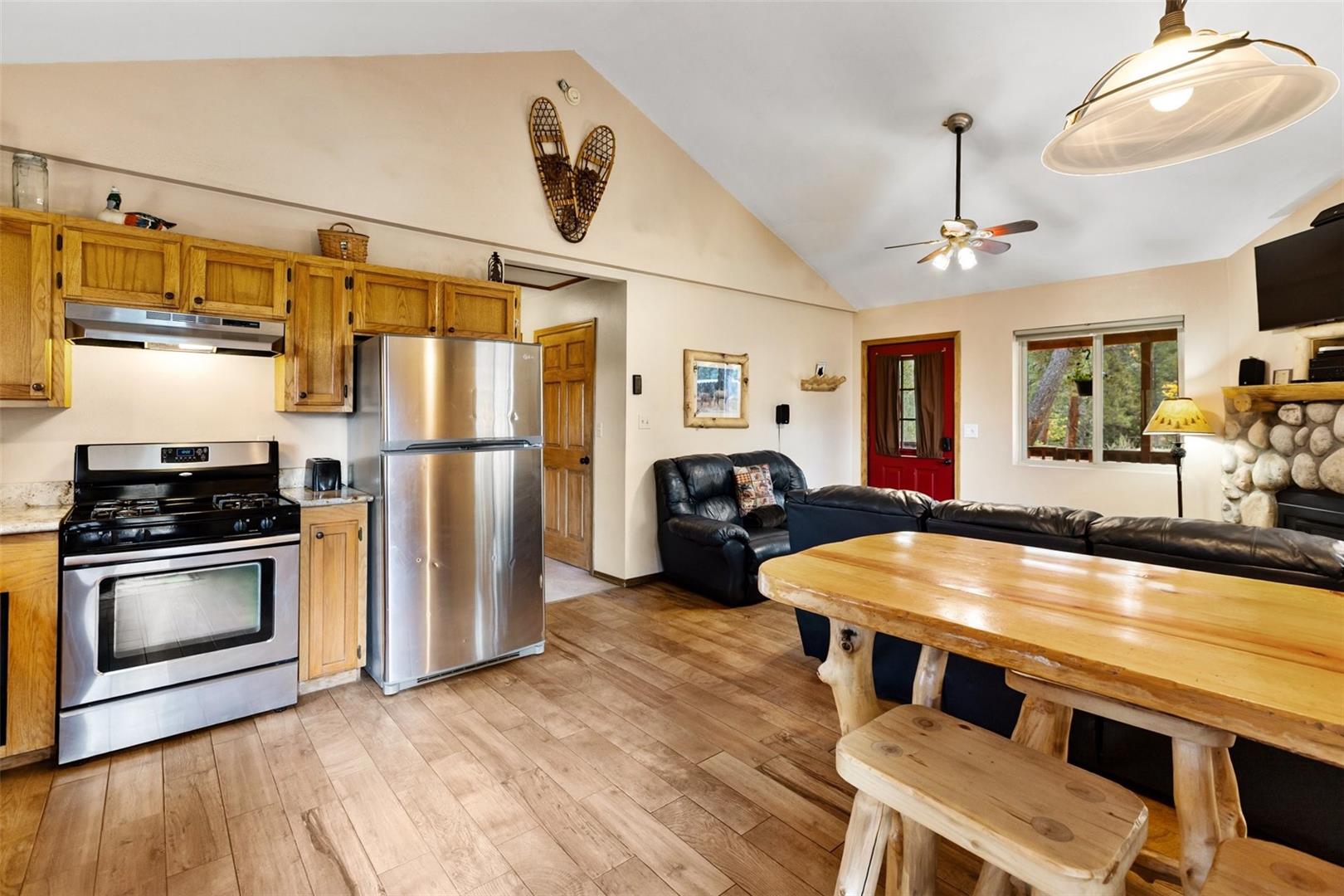 Open-concept living space with vaulted ceilings, wood-finish flooring, and a stone fireplace