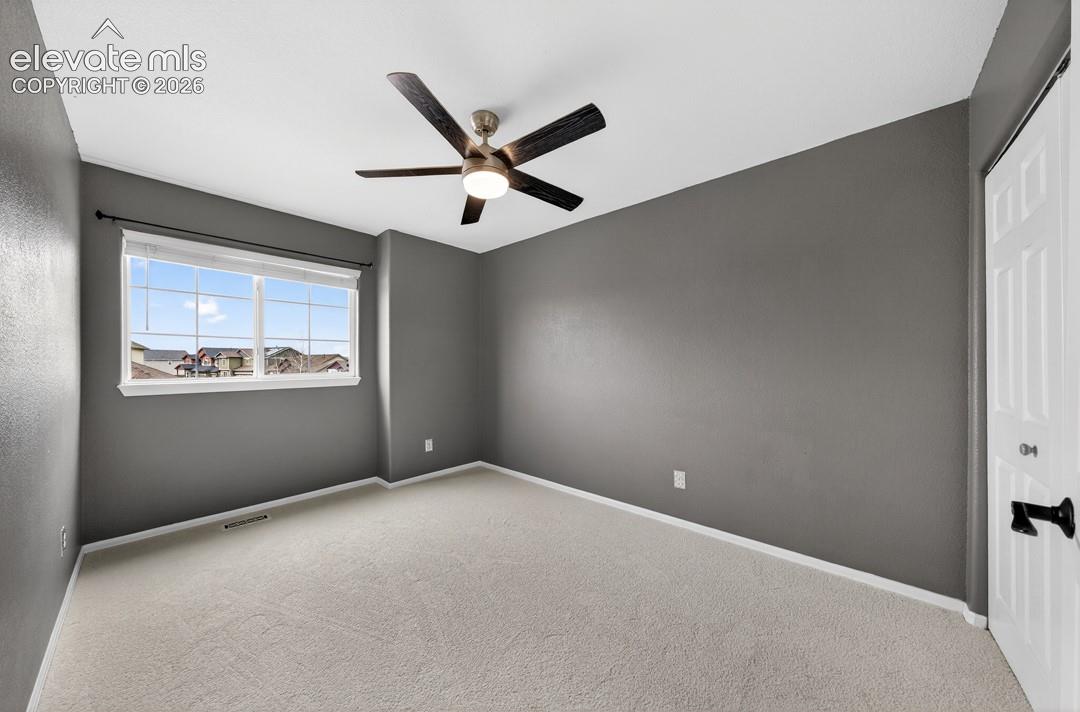 Neutral-toned interior space featuring light-colored wall-to-wall carpeting, grey wall paint, a multi-blade ceiling fan with integrated lighting, and a six-panel closet door