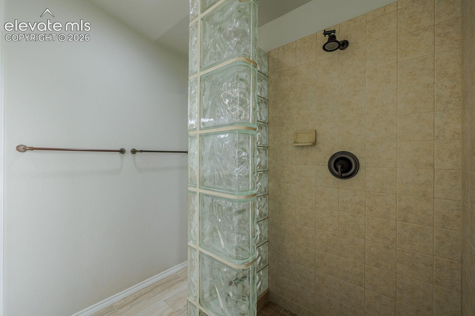 Spa-inspired primary bathroom featuring a custom glass block shower enclosure with decorative patterned panels, dual chrome towel bars, and a rainfall showerhead with matching wall-mounted fixtures