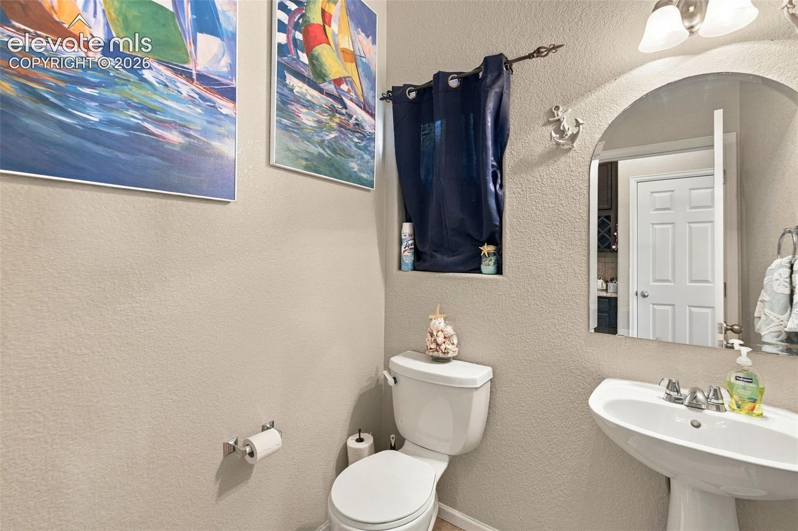 Arched wall mirror, pedestal sink with polished chrome hardware, and wall-mounted light fixture