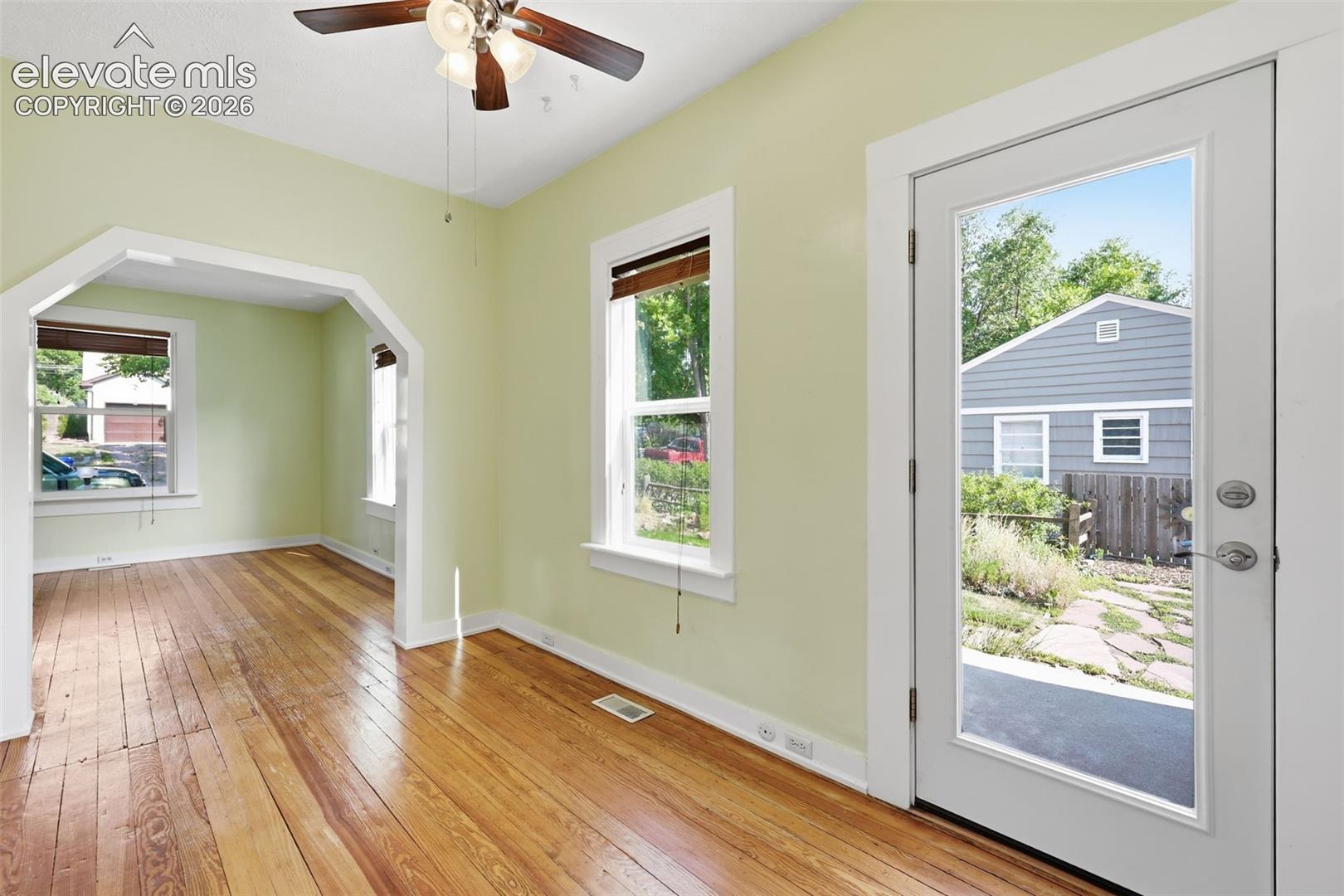 Dining area with pine hardwood flooring, arched opening, a ceiling fan, wooden blinds, white trim, and a glass-paneled side door.