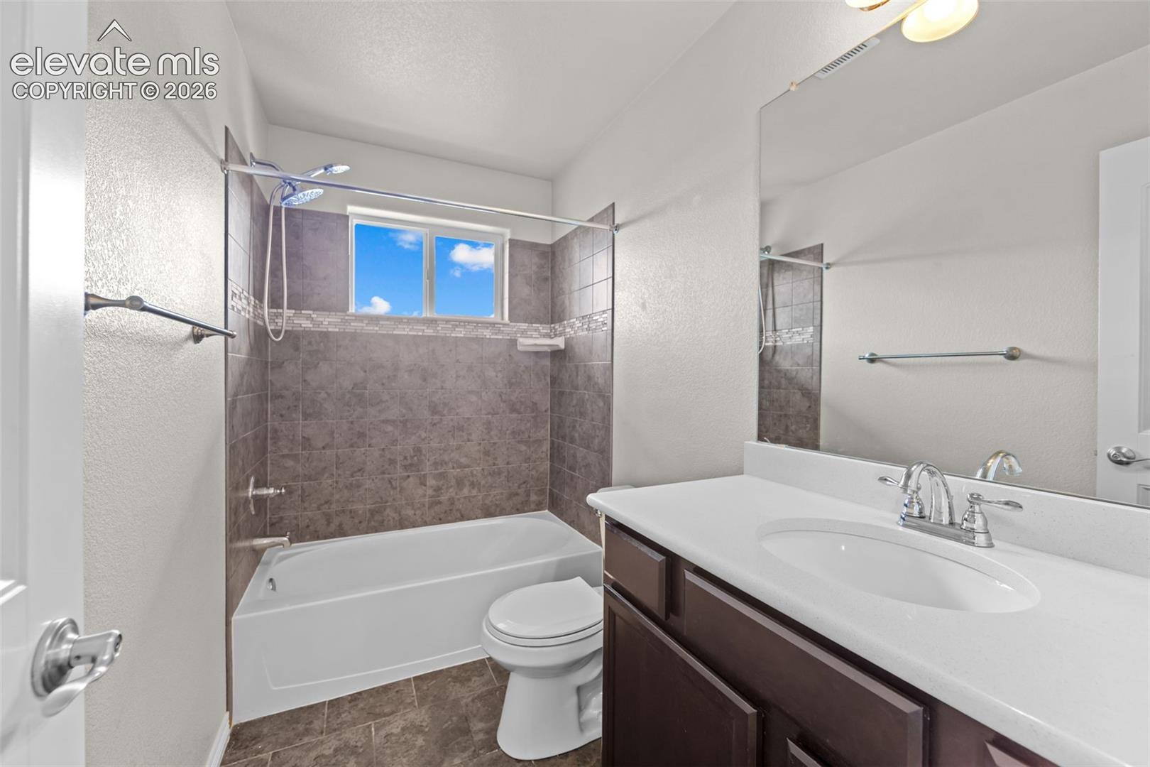 Bathroom featuring a shower/tub combination with tiled surround, a window providing natural light, a single vanity with a white countertop, and a large wall-mounted mirror