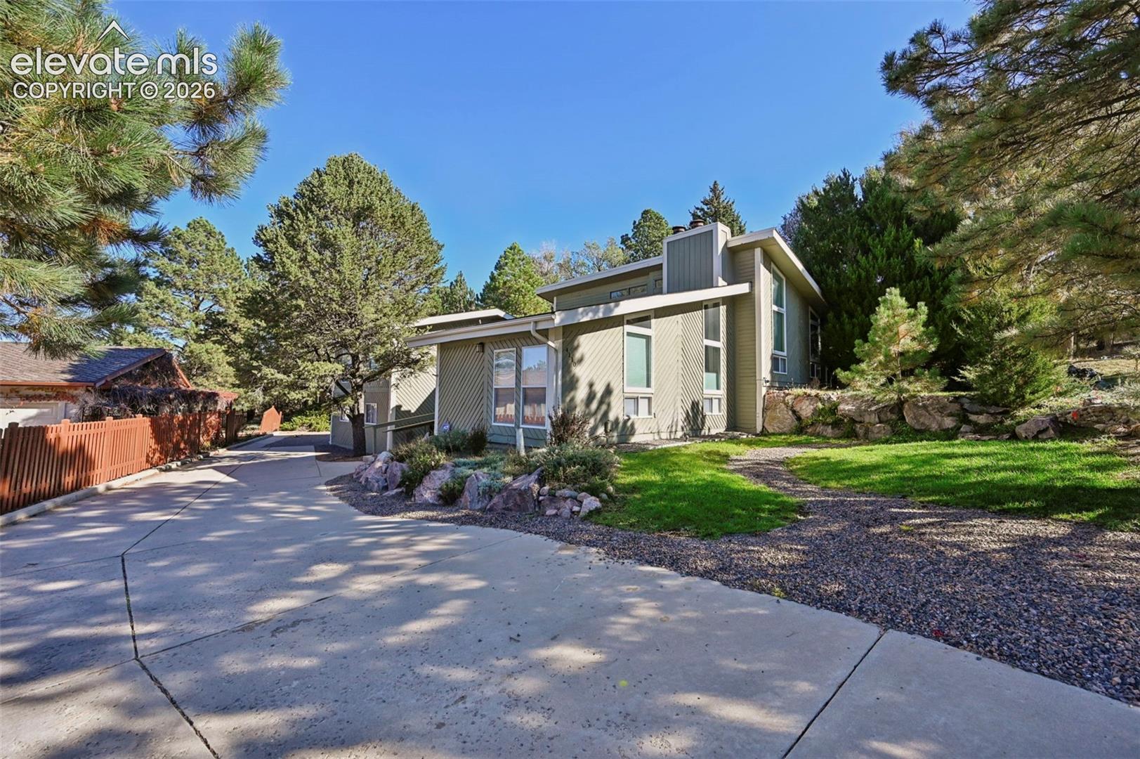 Contemporary exterior featuring vertical siding, geometric roof lines, a concrete driveway, multi-level stone retaining walls, and mature coniferous landscaping