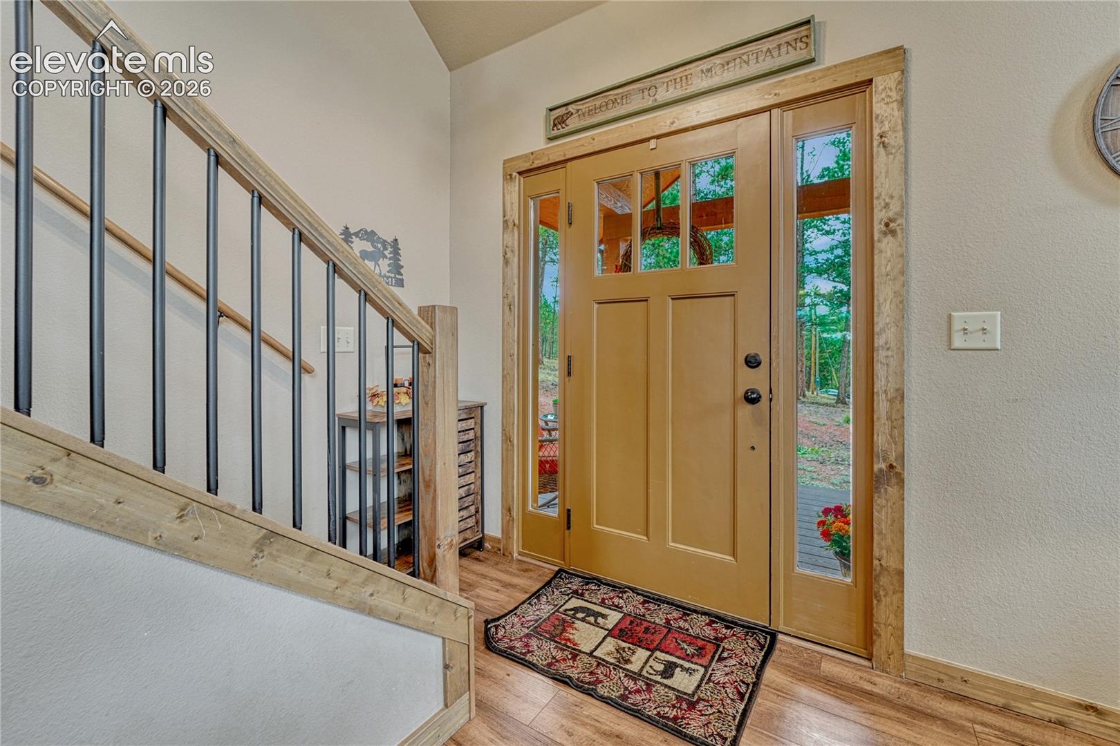 Entryway featuring a solid wood front door with glass sidelights, rustic wood trim, wood-finish flooring, and a staircase with metal balusters