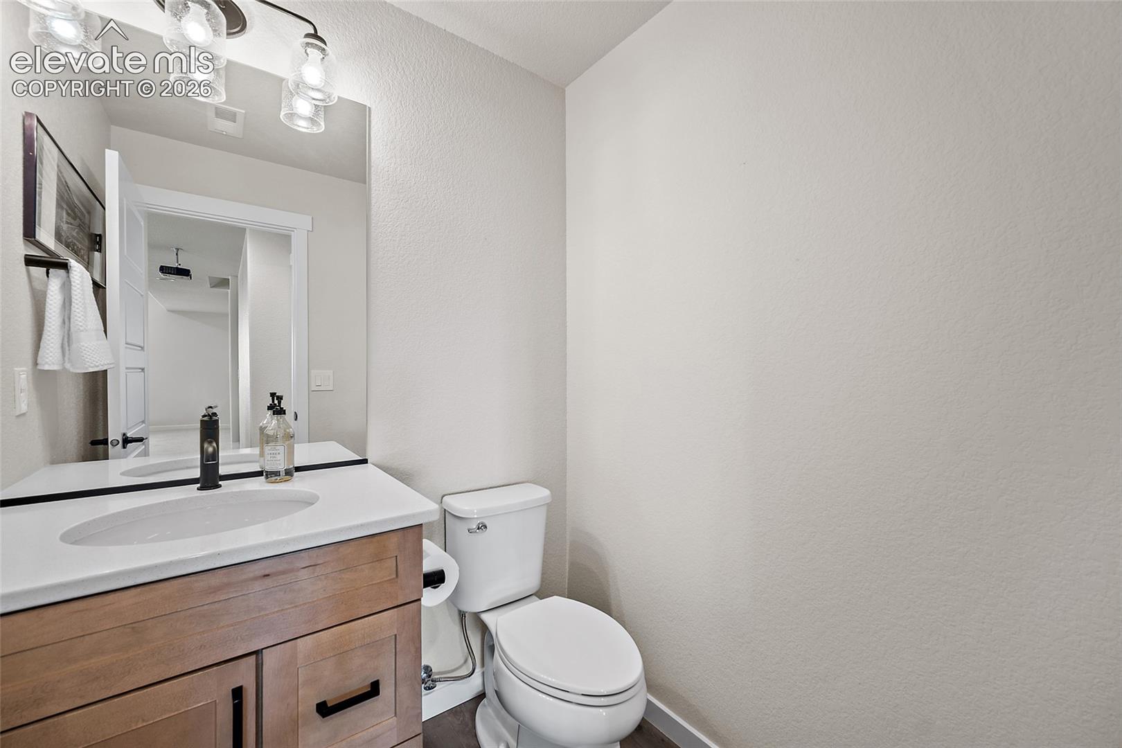 Wood-finish vanity with black hardware, white countertop with integrated sink, contemporary black faucet, and modern vanity lighting
