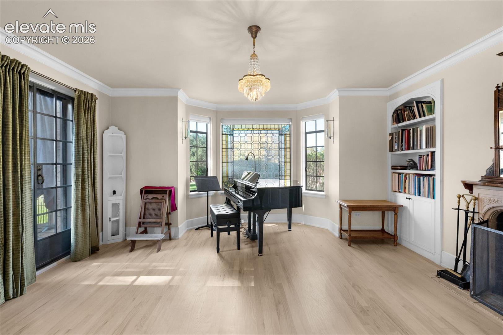 Bay window with leaded glass accents, built-in recessed shelving, fireplace with an ornate mantel, crown molding, and crystal chandelier