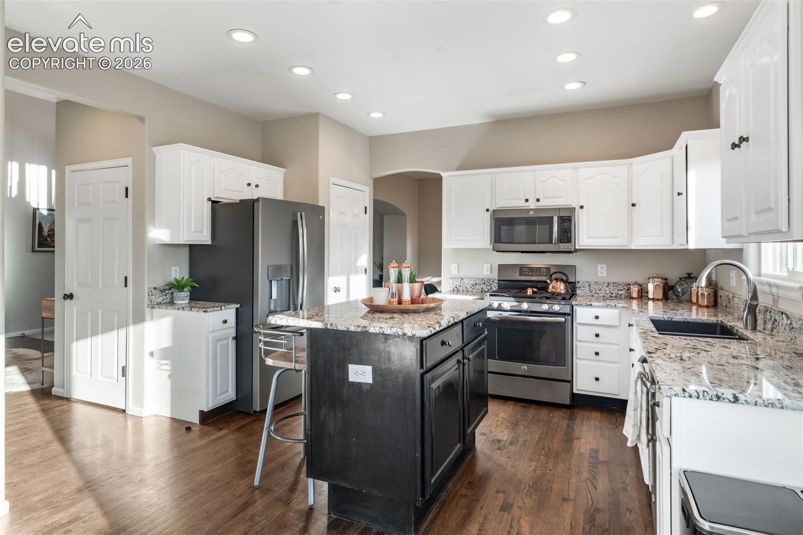 Kitchen featuring white upper cabinetry, a black center island, stone-finish countertops, recessed lighting, and wood-finish flooring