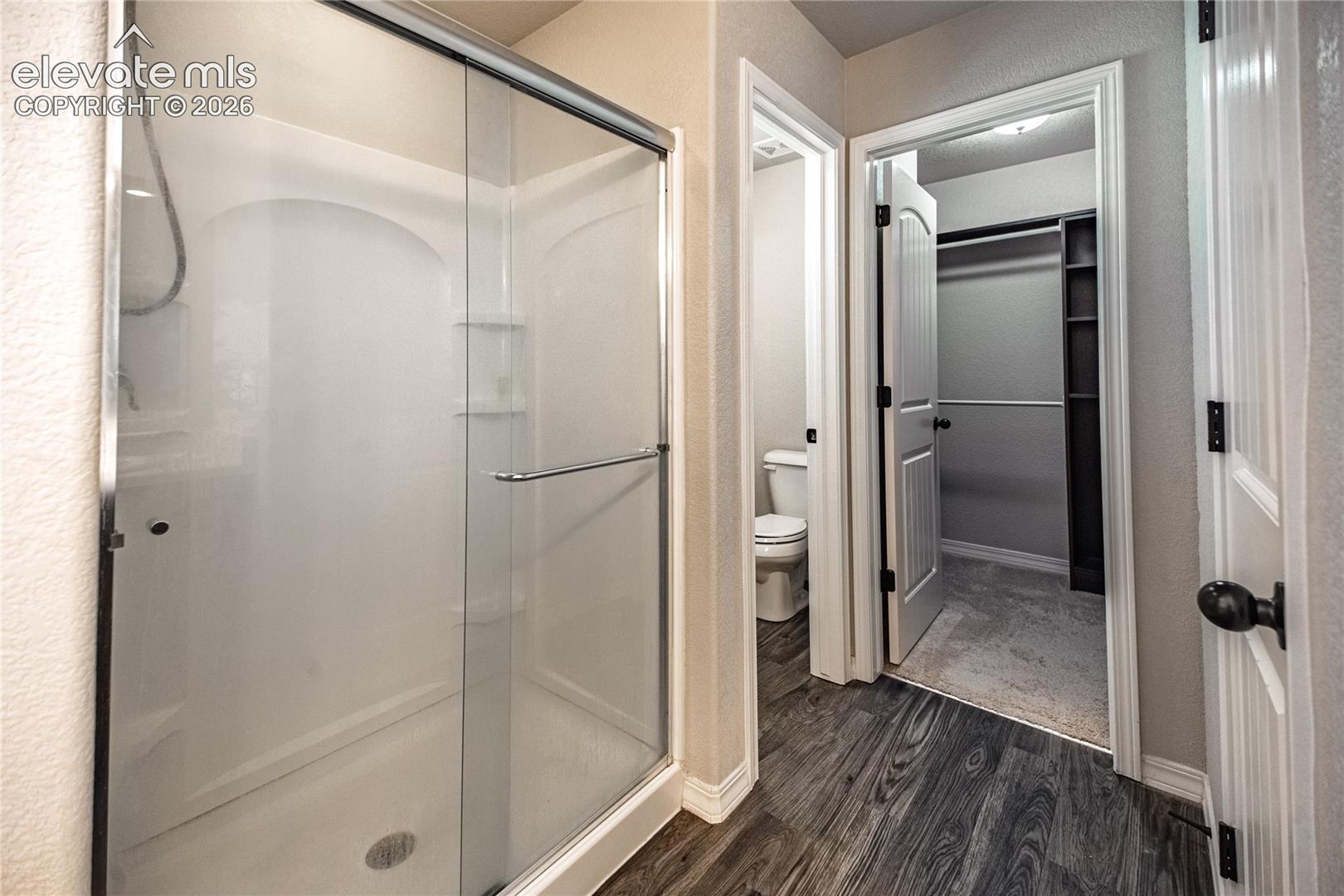 Glass-enclosed shower with integrated shelving, wood-finish flooring, and built-in closet shelving