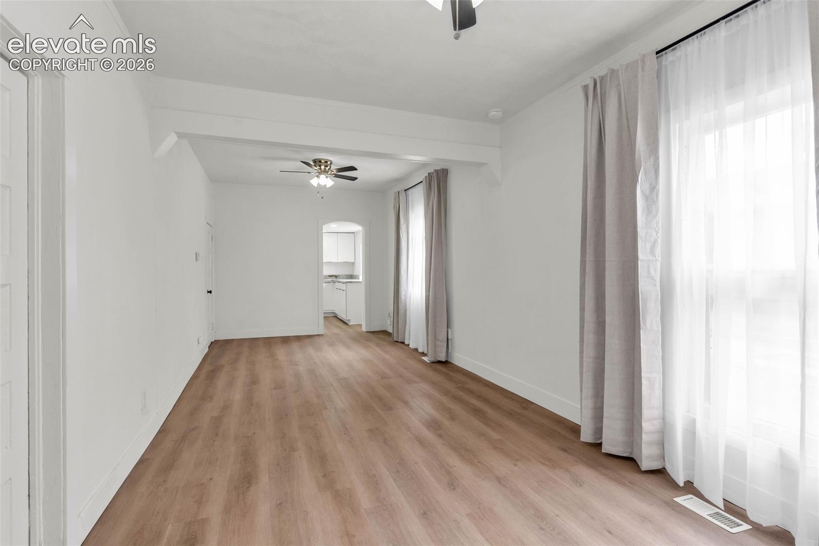 Neutral interior featuring wood-finish flooring, ceiling-mounted light fixtures with fans, and an arched doorway
