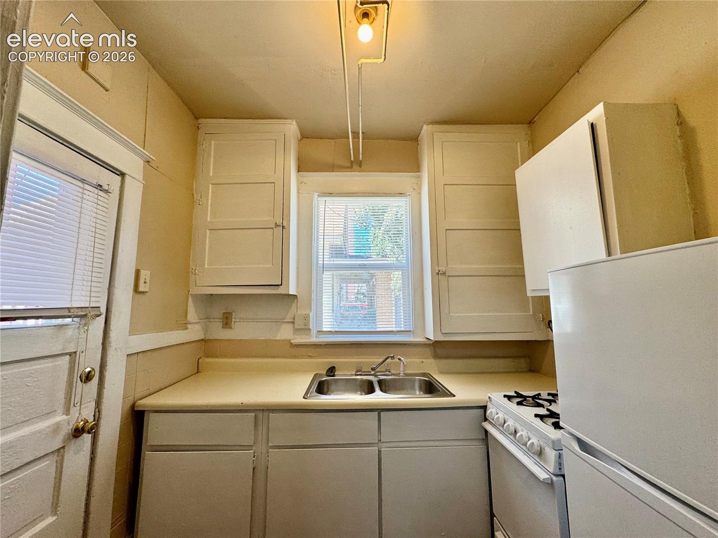 Kitchen featuring a double basin sink, window, white cabinetry, and white appliances