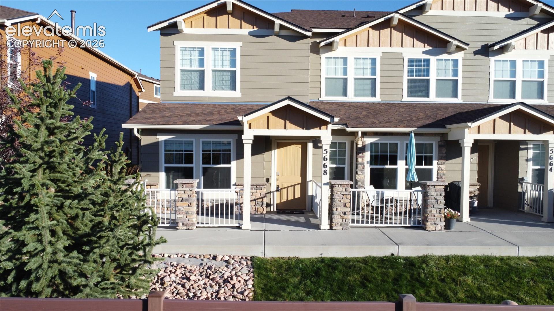 Two-story exterior featuring horizontal siding, decorative gable accents, covered front porch, stone-clad porch columns, and a concrete patio