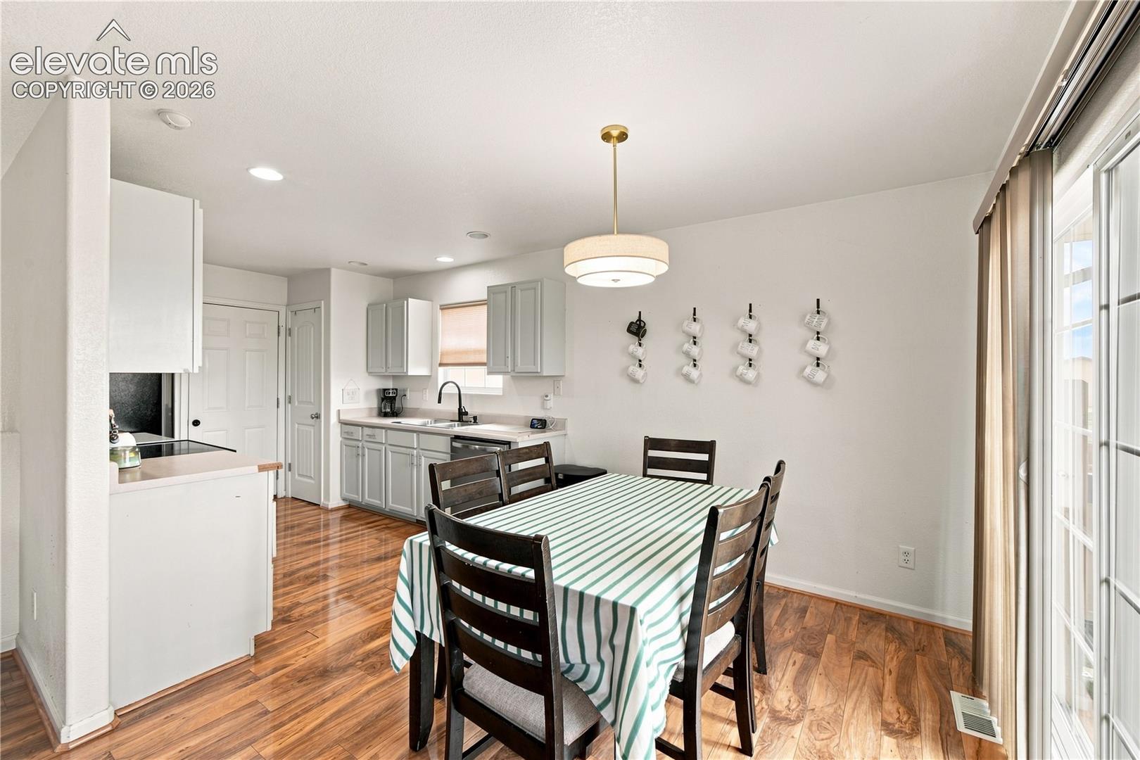 Kitchen and dining area featuring wood-finish flooring, white walls, and a contemporary pendant light fixture