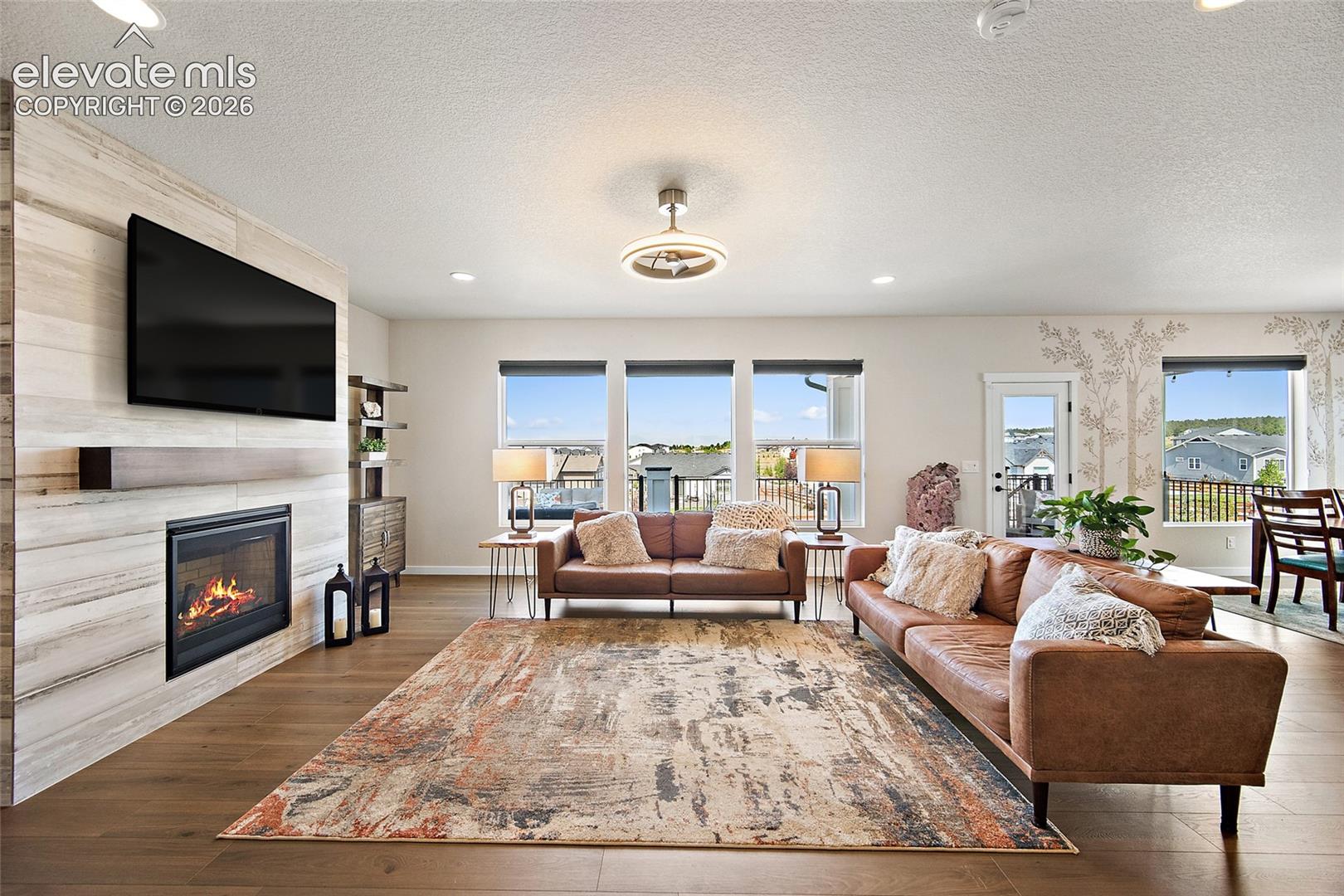 Spacious living area featuring wood-finish flooring, a contemporary fireplace with a stone-panel surround, recessed lighting, and multiple windows