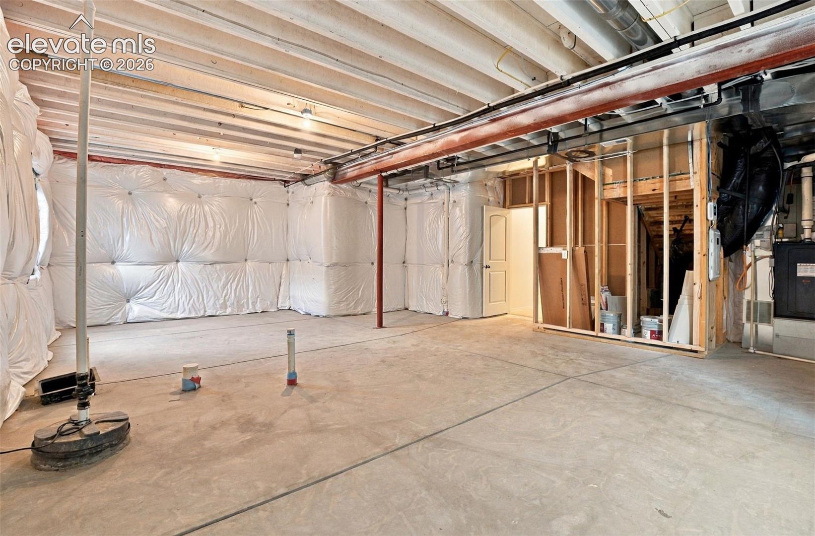 Unfinished lower level featuring concrete flooring, exposed ceiling joists, plastic vapor-barrier wall insulation, and rough-in plumbing