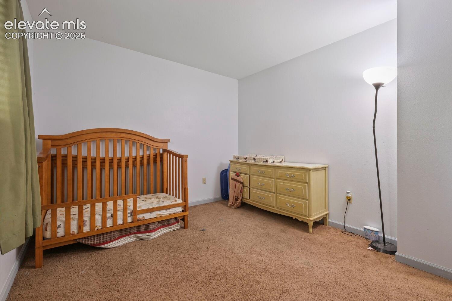 Carpeted room featuring white walls and a window with light green curtains