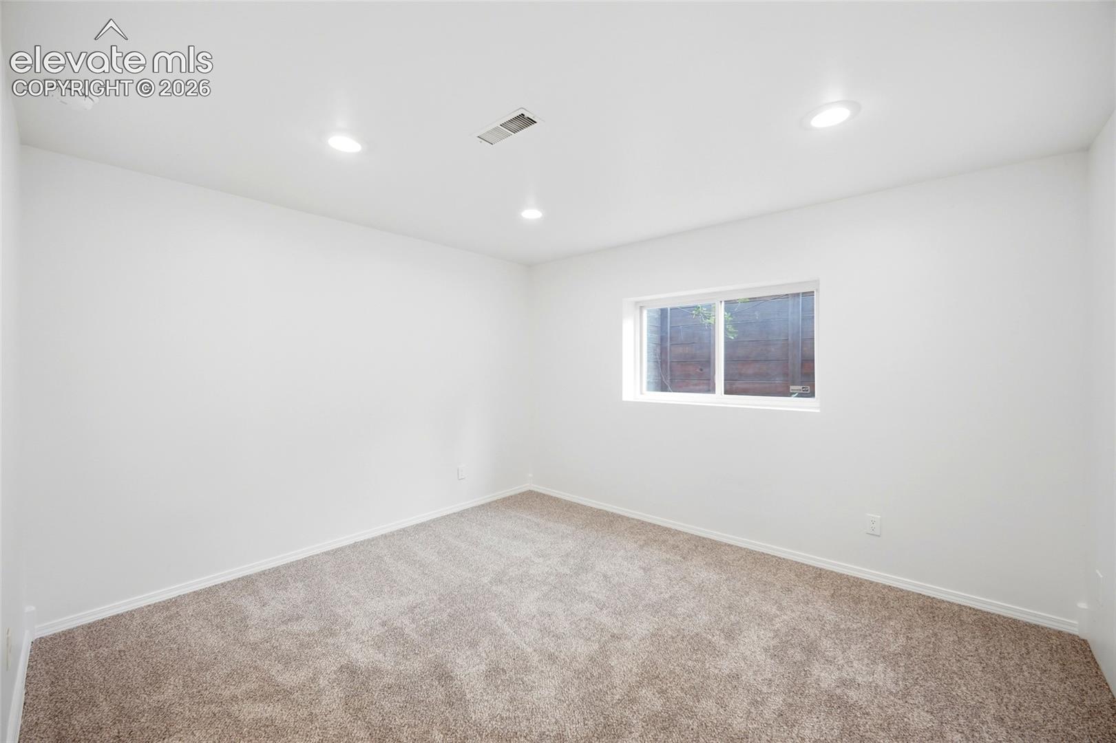 Neutral-toned wall-to-wall carpeting, recessed ceiling lighting, and a single-pane slider window
