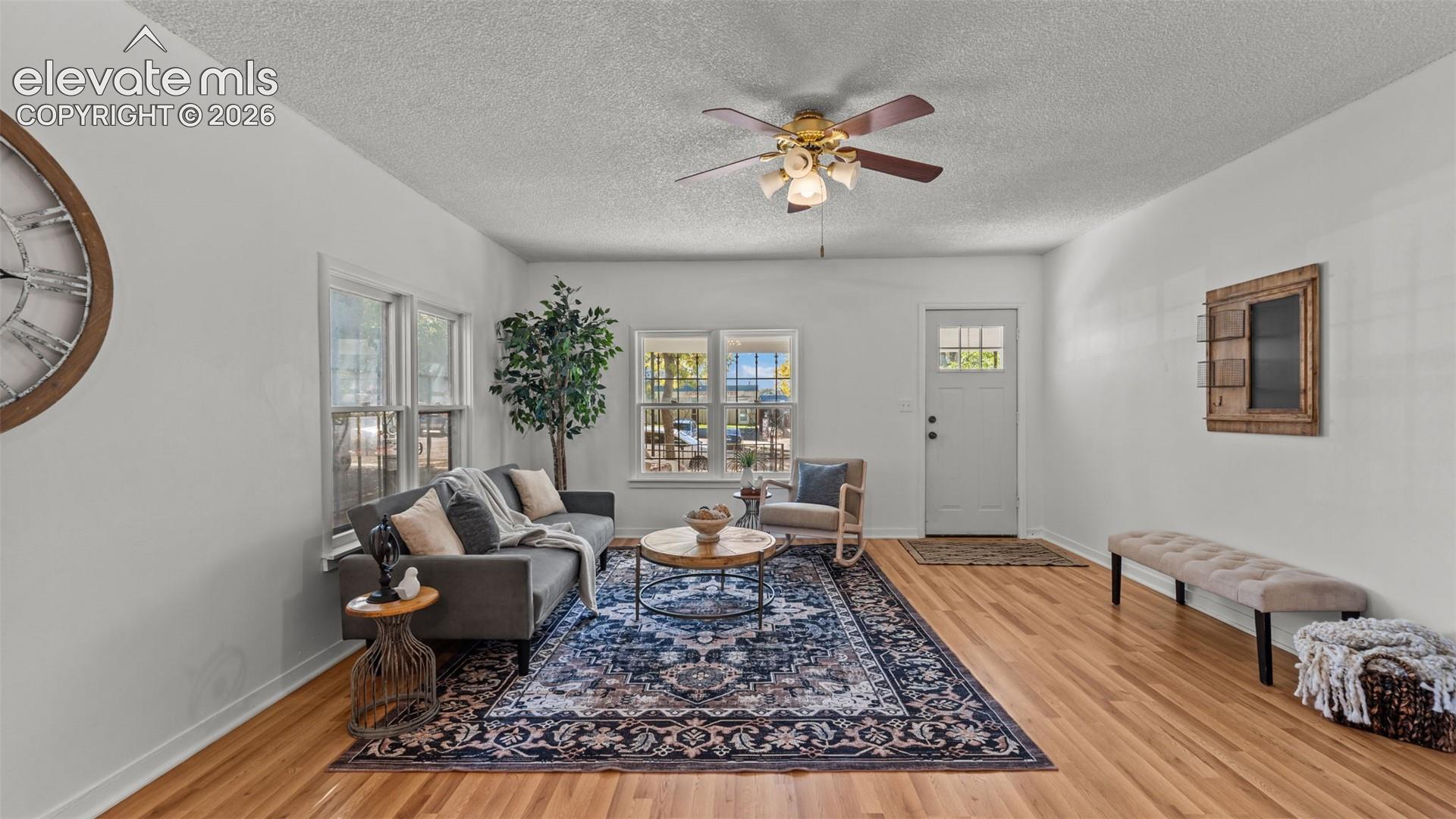 Hardwood flooring, multiple windows, ceiling fan, white paneled door with window inserts, and light-colored walls