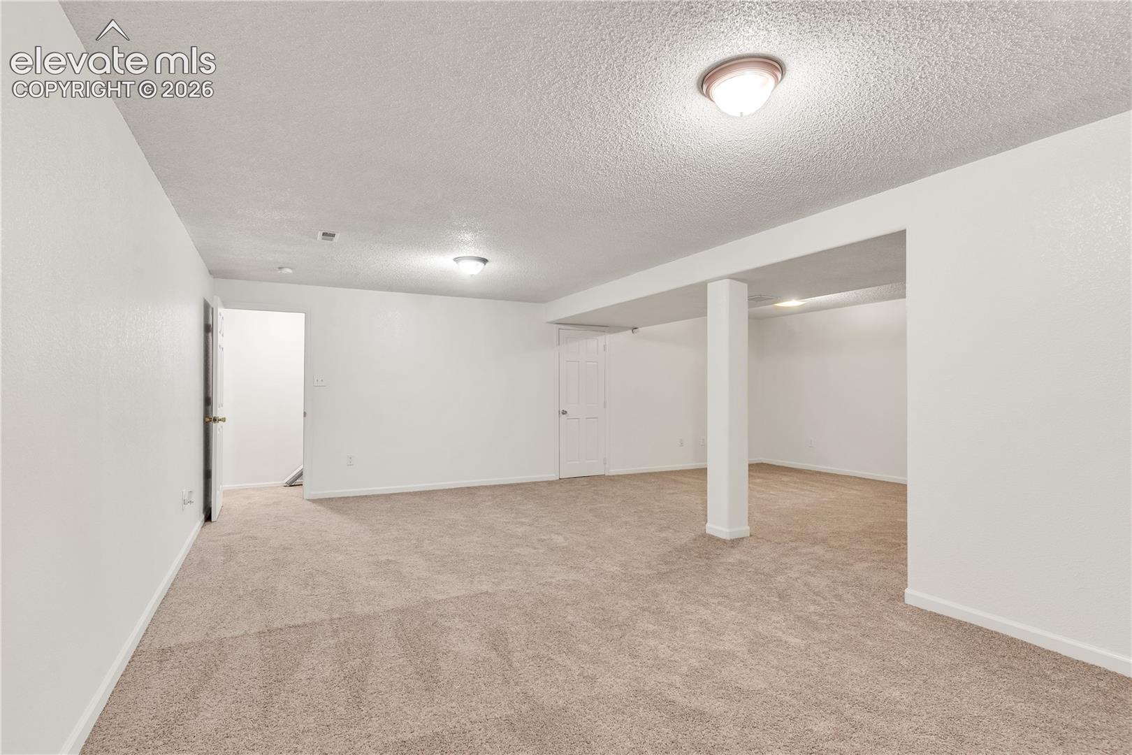 Neutral carpet flooring, white painted walls, ceiling-mounted lighting, and a structural support column