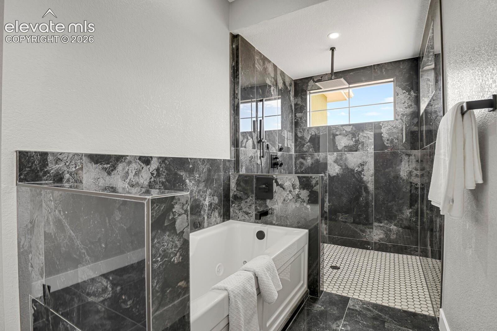 Bathroom featuring a deep soaking tub, walk-in shower with large-format stone-finish wall tiles, hexagon tile flooring, and matte black fixtures