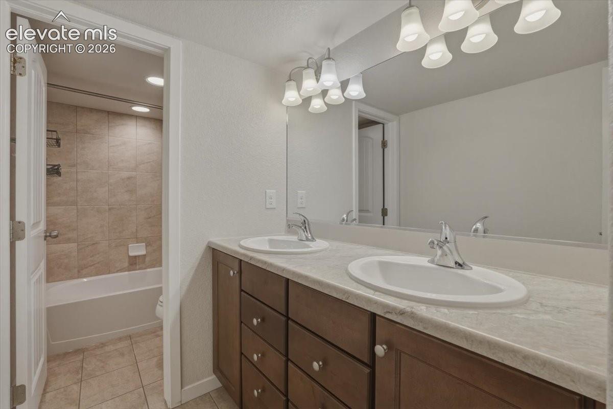 Bathroom featuring a double vanity with integrated sinks, a wood-finish cabinet with drawers, a large wall-mounted mirror, and a multi-bulb vanity light fixture