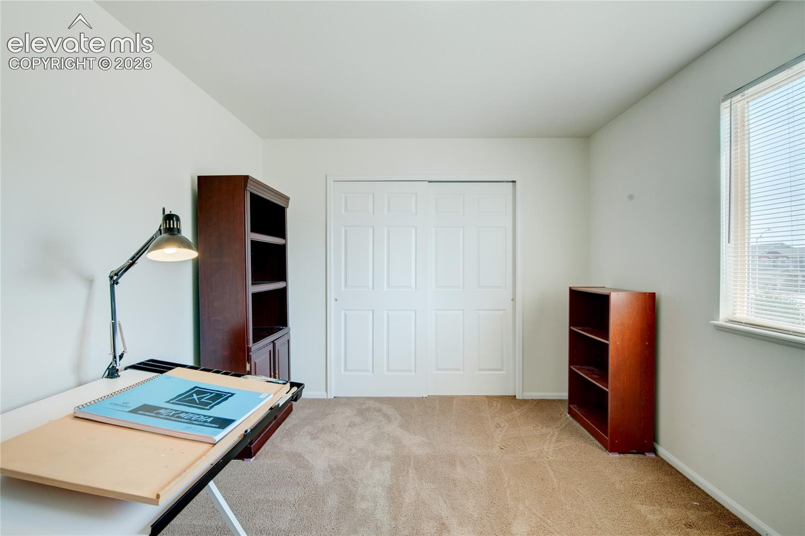 Carpeted room featuring a double-door closet with paneled doors, a window with horizontal blinds, and neutral wall tones