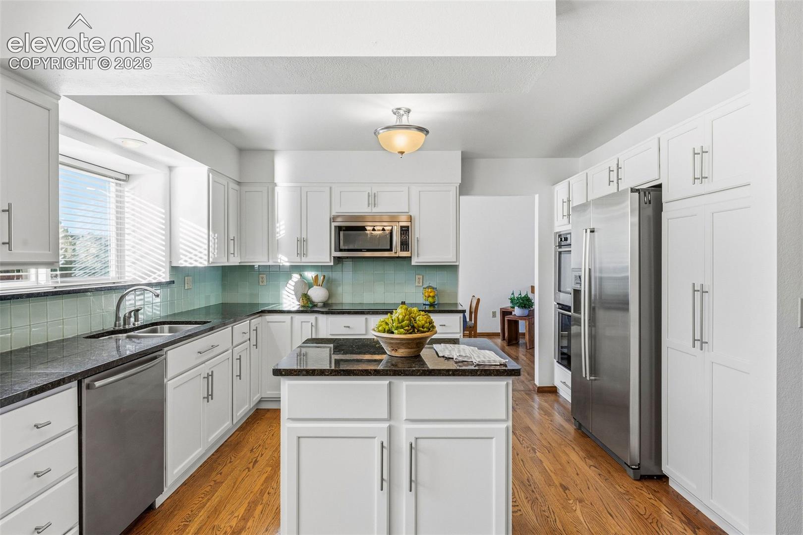 Kitchen featuring white cabinetry with silver-tone hardware, dark stone-finish countertops, stainless steel appliances, a center island, and wood-finish flooring