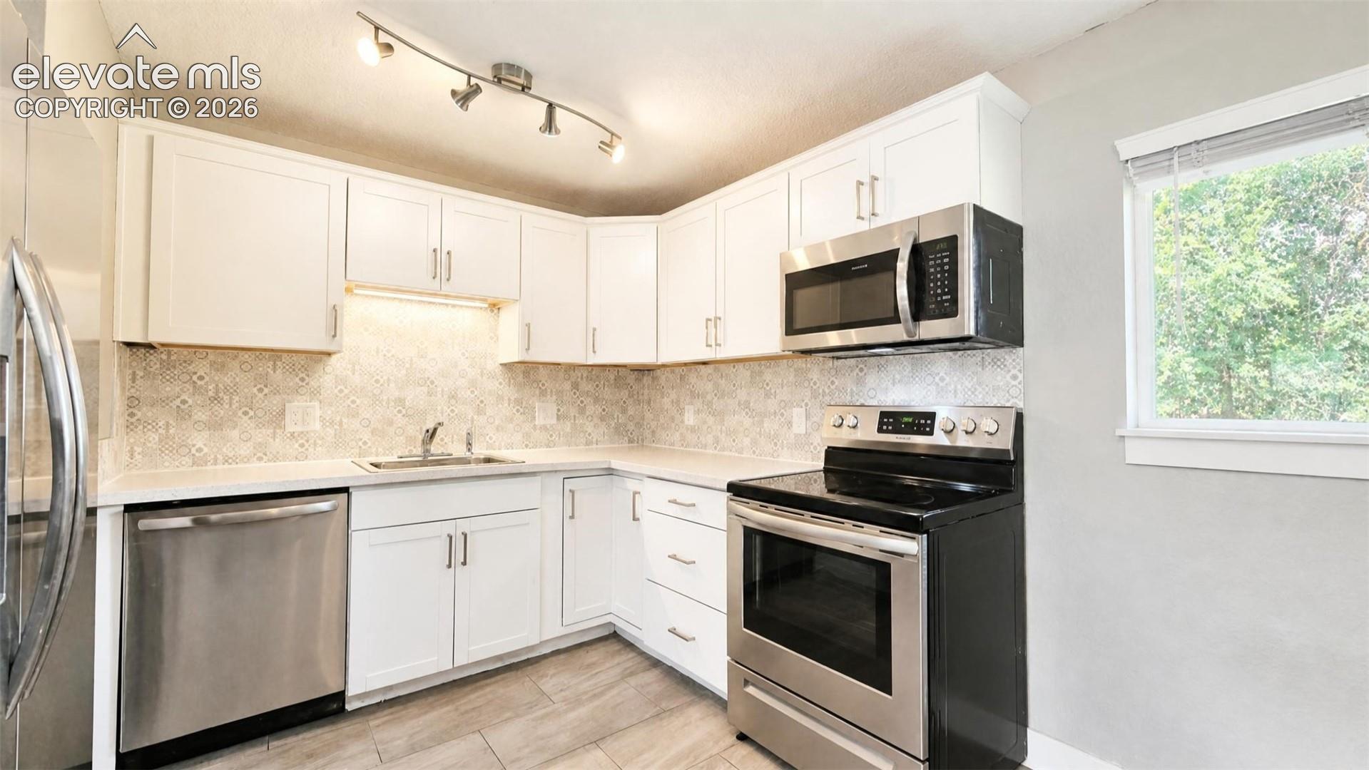 Kitchen featuring white cabinetry, stainless steel appliances, a tile backsplash, and LVP flooring