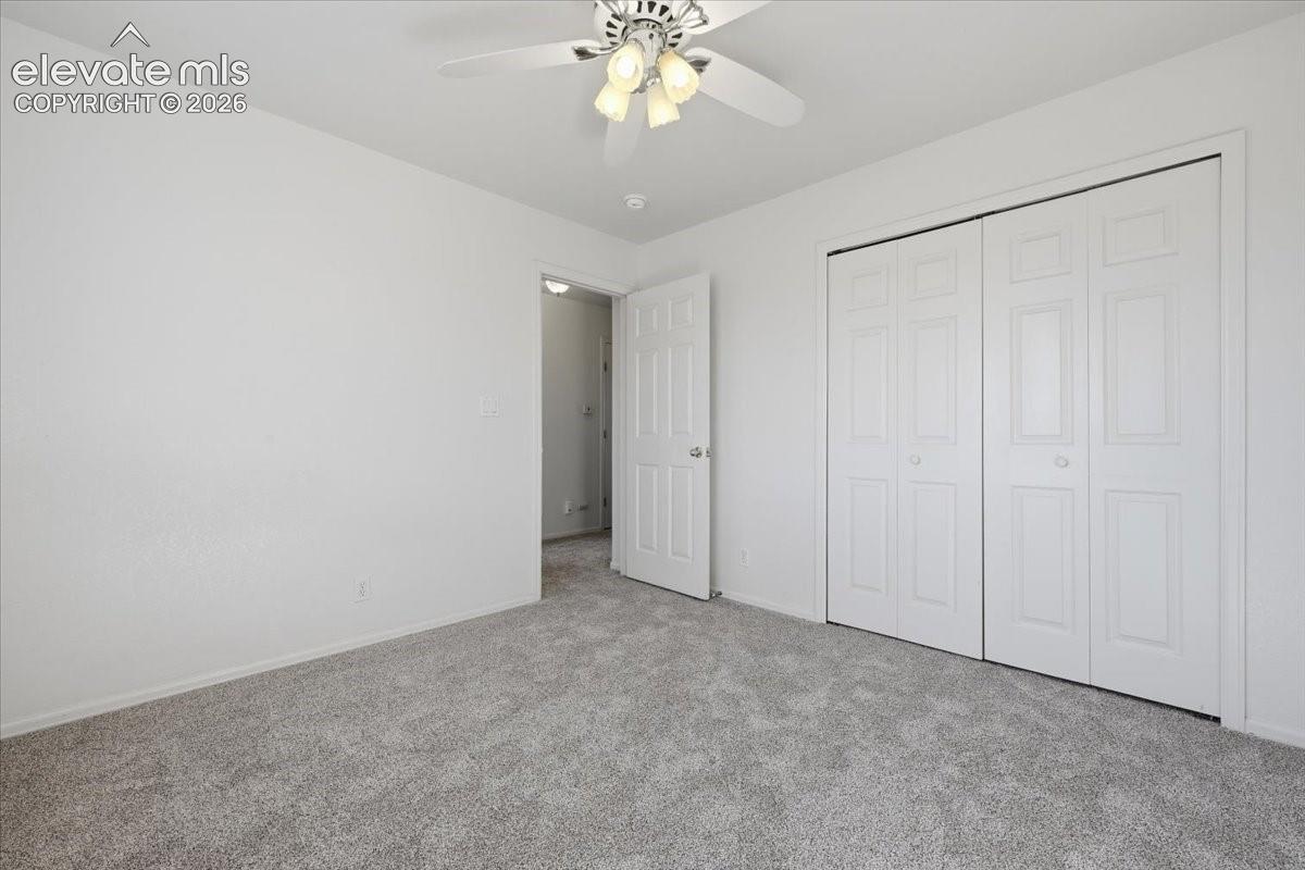 White walls, light gray carpeting, ceiling fan with integrated lighting, and bi-fold closet doors