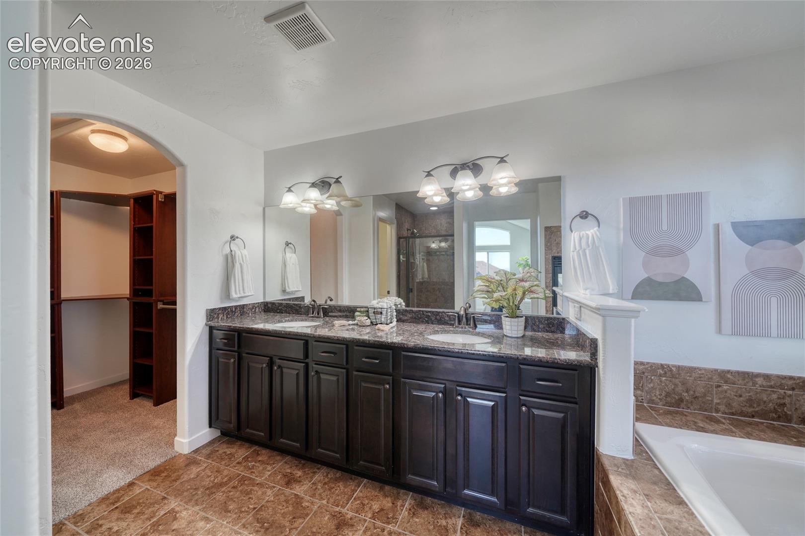 Dual sink vanity with dark wood-finish cabinetry, stone countertop, and tile flooring