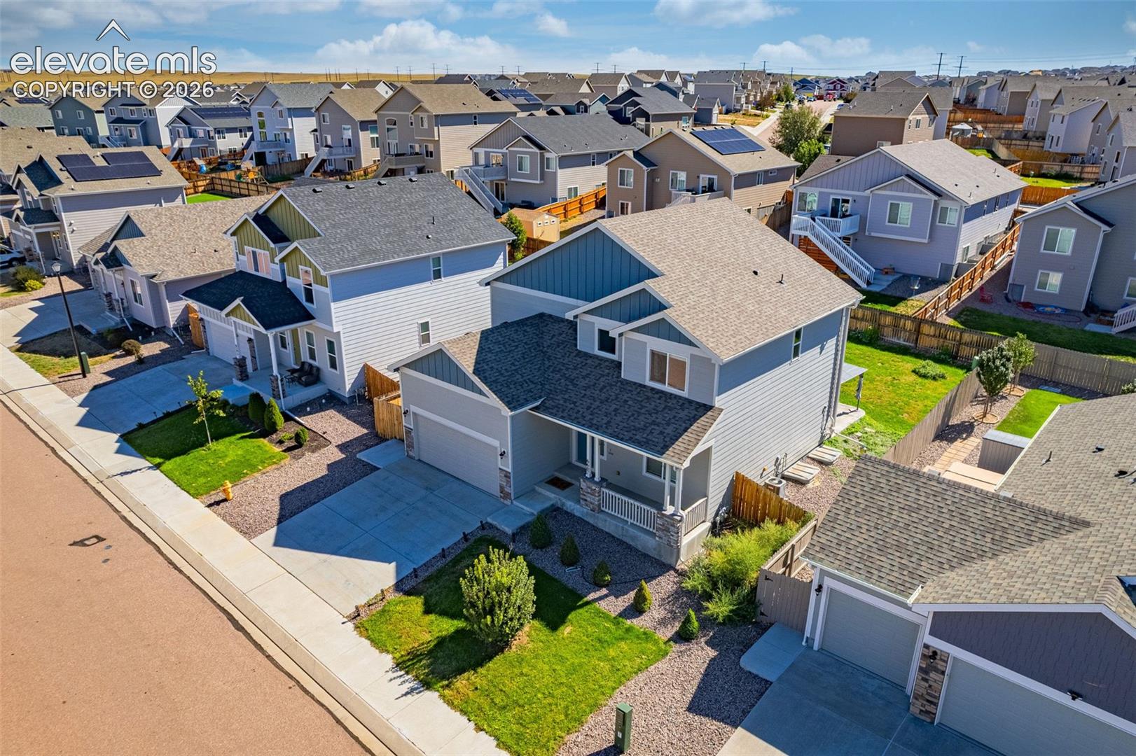 Exterior featuring gray siding with blue accents, an attached garage, a covered front porch, and a landscaped front yard