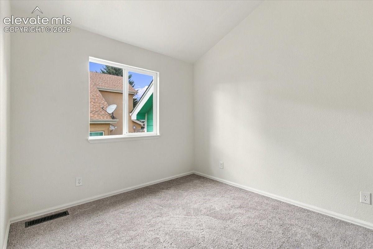 Neutral-toned room featuring a vaulted ceiling, neutral wall-to-wall carpeting, and a double-pane window