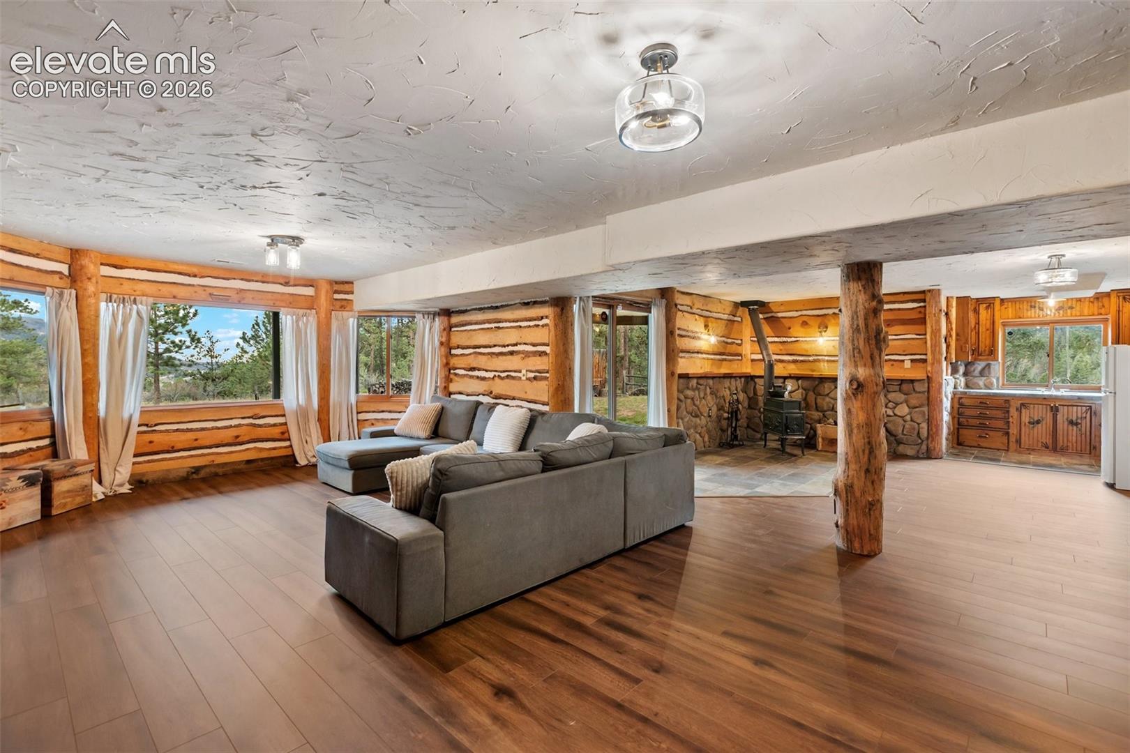 Interior featuring exposed log walls, wood-finish flooring, a stone-surround fireplace, a structural log pillar, and built-in cabinetry