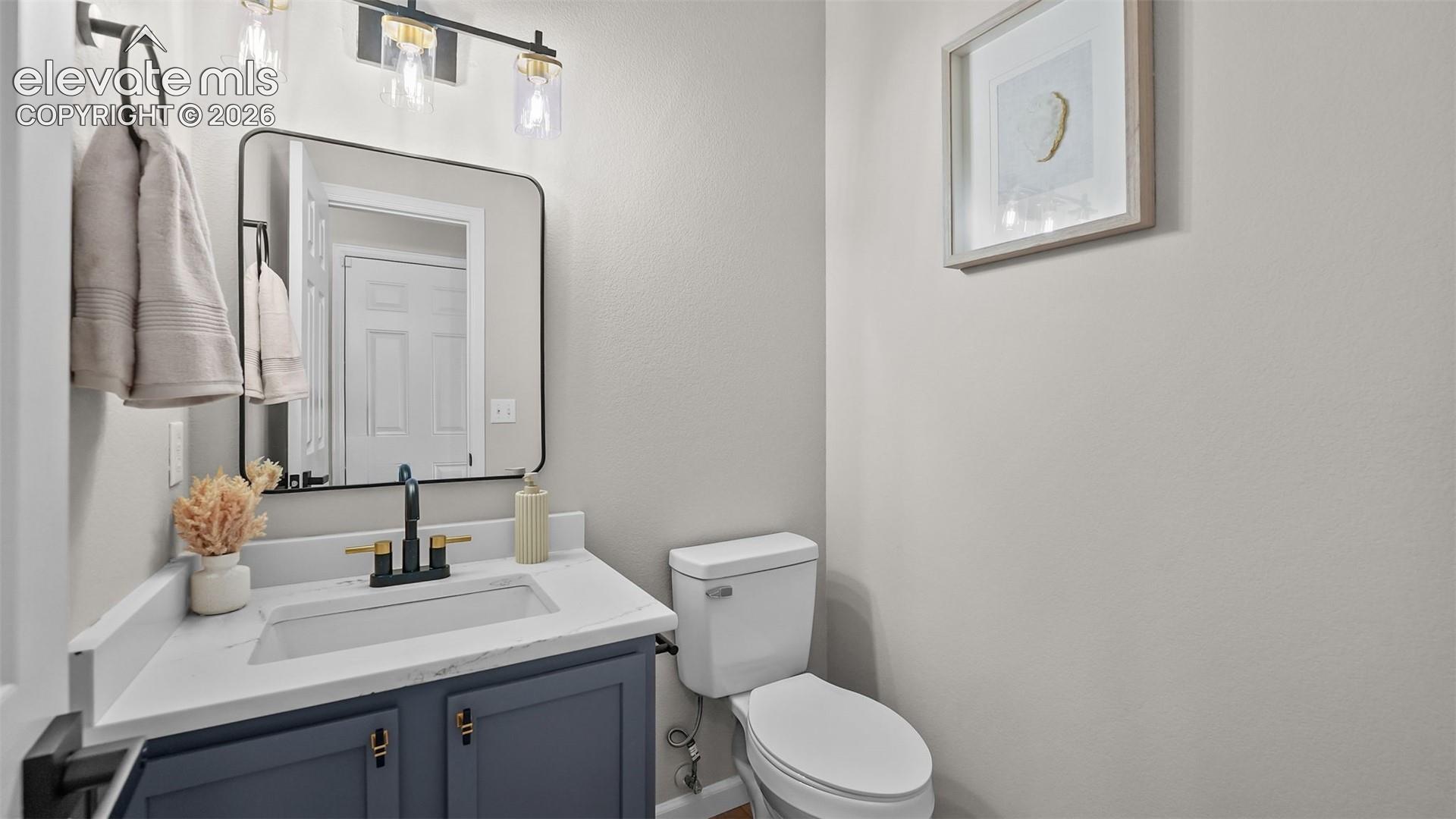 Vanity with a white countertop and integrated sink, matte black and gold-tone faucet, and a wall-mounted rectangular mirror