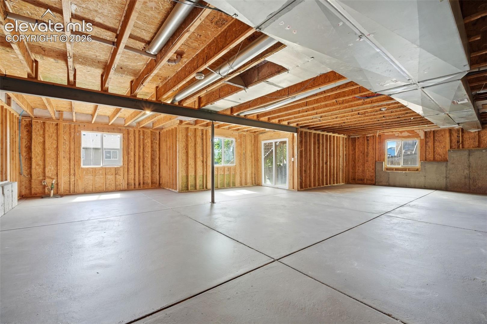 Unfinished basement featuring exposed wood framing, concrete flooring, multiple windows, and a sliding glass door