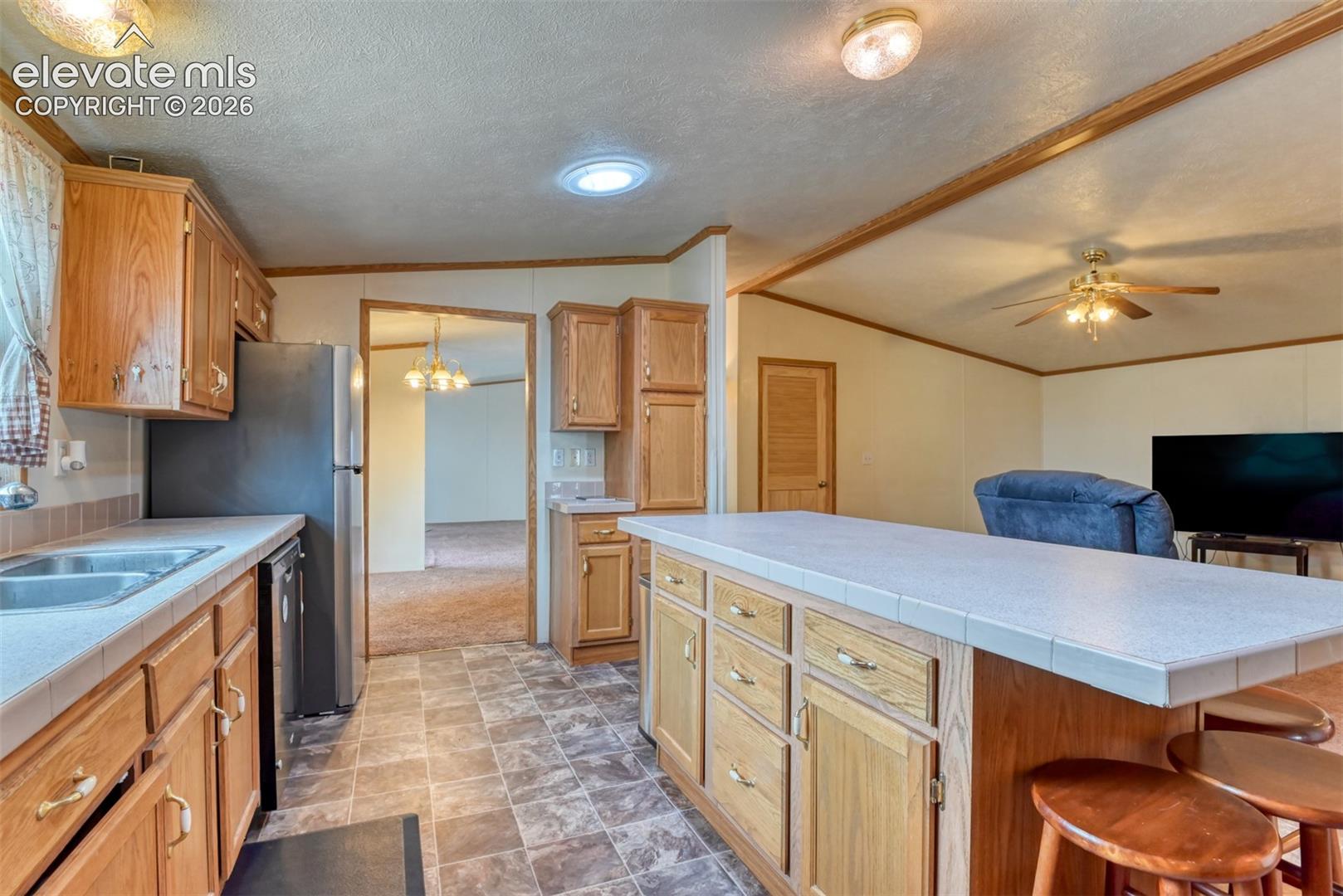 Kitchen featuring wood cabinetry, tiled countertops, a stainless steel refrigerator, and a double basin sink