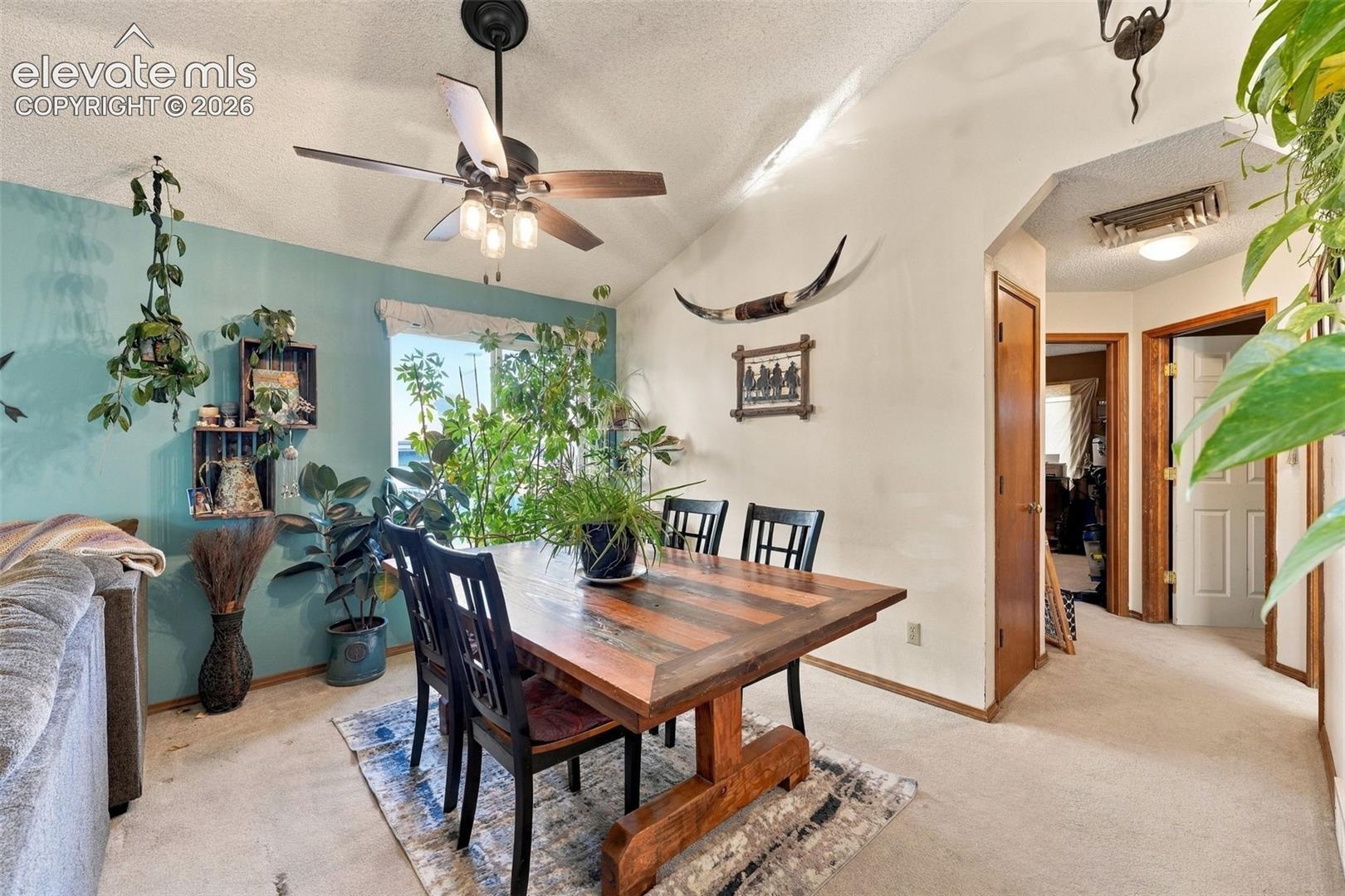 Vaulted ceiling featuring a central multi-blade ceiling fan with integrated light kit, complemented by natural lighting through a picture window