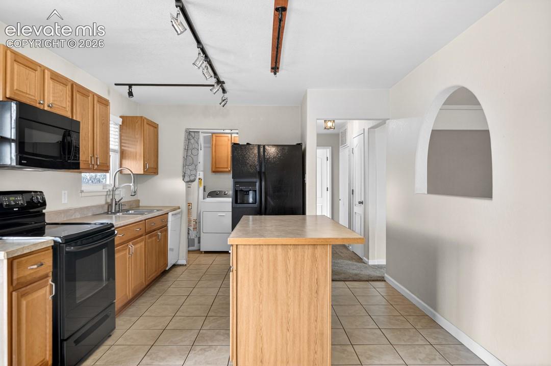 Kitchen featuring wood cabinetry, black appliances, track lighting, a central island, and tiled flooring