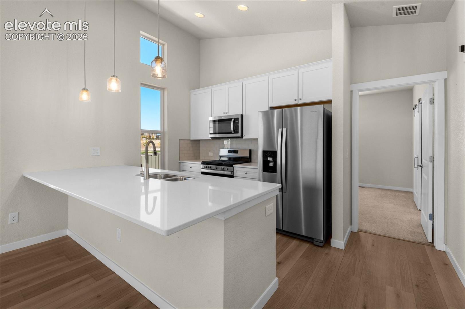 Kitchen featuring white cabinetry, quartz countertops, stainless steel appliances, recessed ceiling lighting, and wood-finish flooring